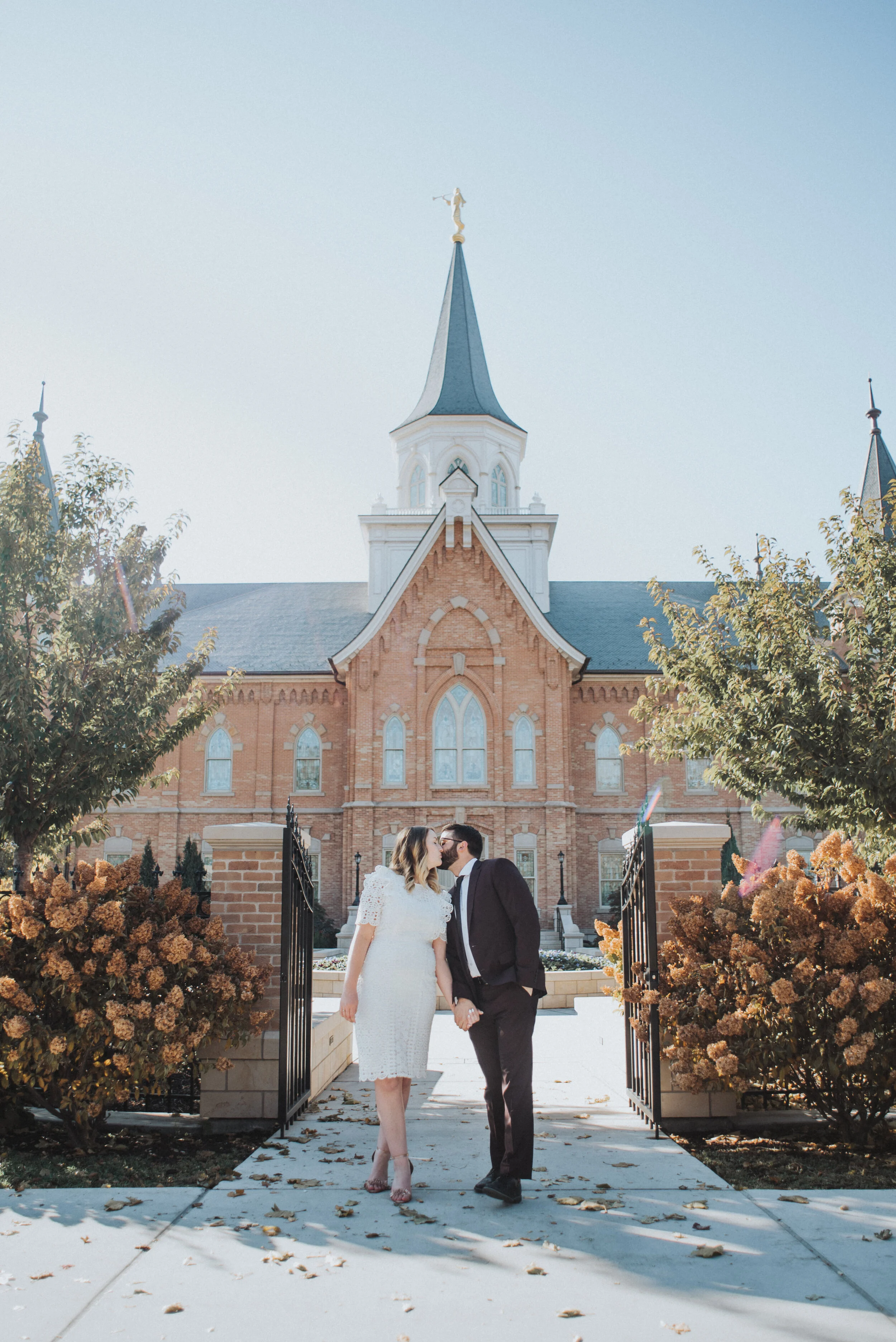 provo city center temple wedding holding hands walking kissing happy wedding exit formal photos short knee length lace wedding dress modest burgundy wedding suit utah valley professional wedding photography lds provo utah #utahvalleyweddingphotograp