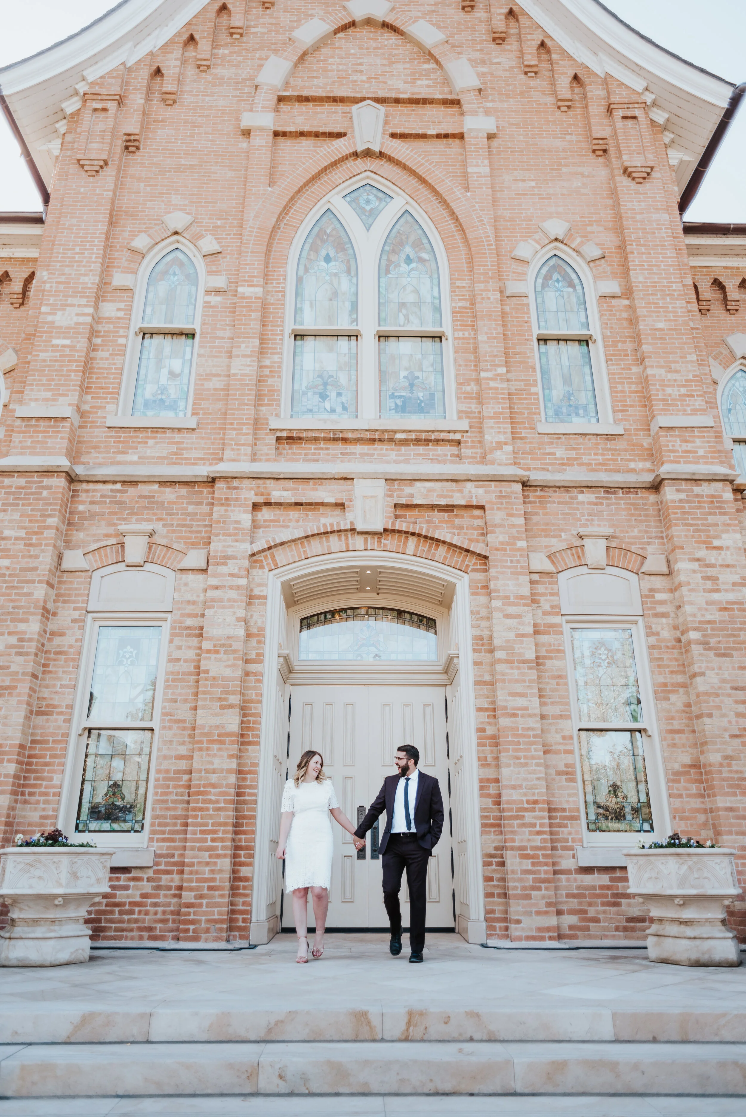  holding hands provo city center lds temple stained glass windows church provo utah professional wedding photographer knee length wedding dress short sleeved modest lace wedding dress burgundy trendy wedding suit happy walking natural posed photograp