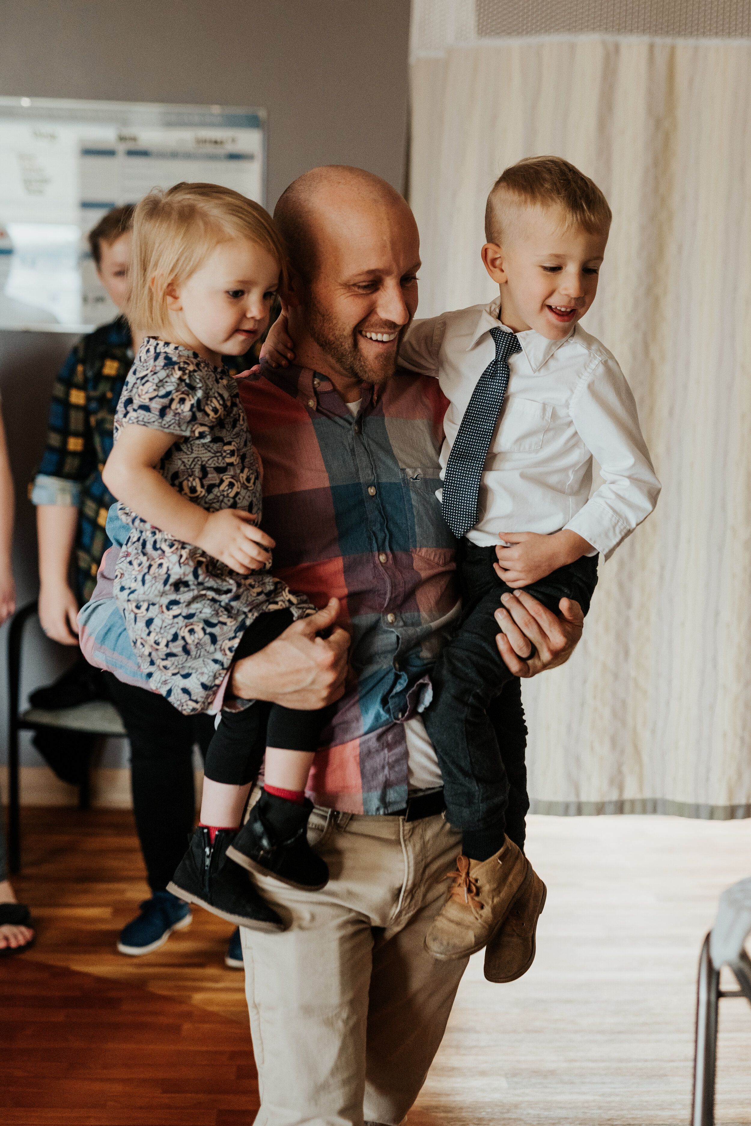  Dad holding the newborn baby’s brother and sister when they meet their new brother for the first time in the hospital. newborn photographer in cache valley logan utah professional birth story photographer hospital pictures of a brand new baby birth 