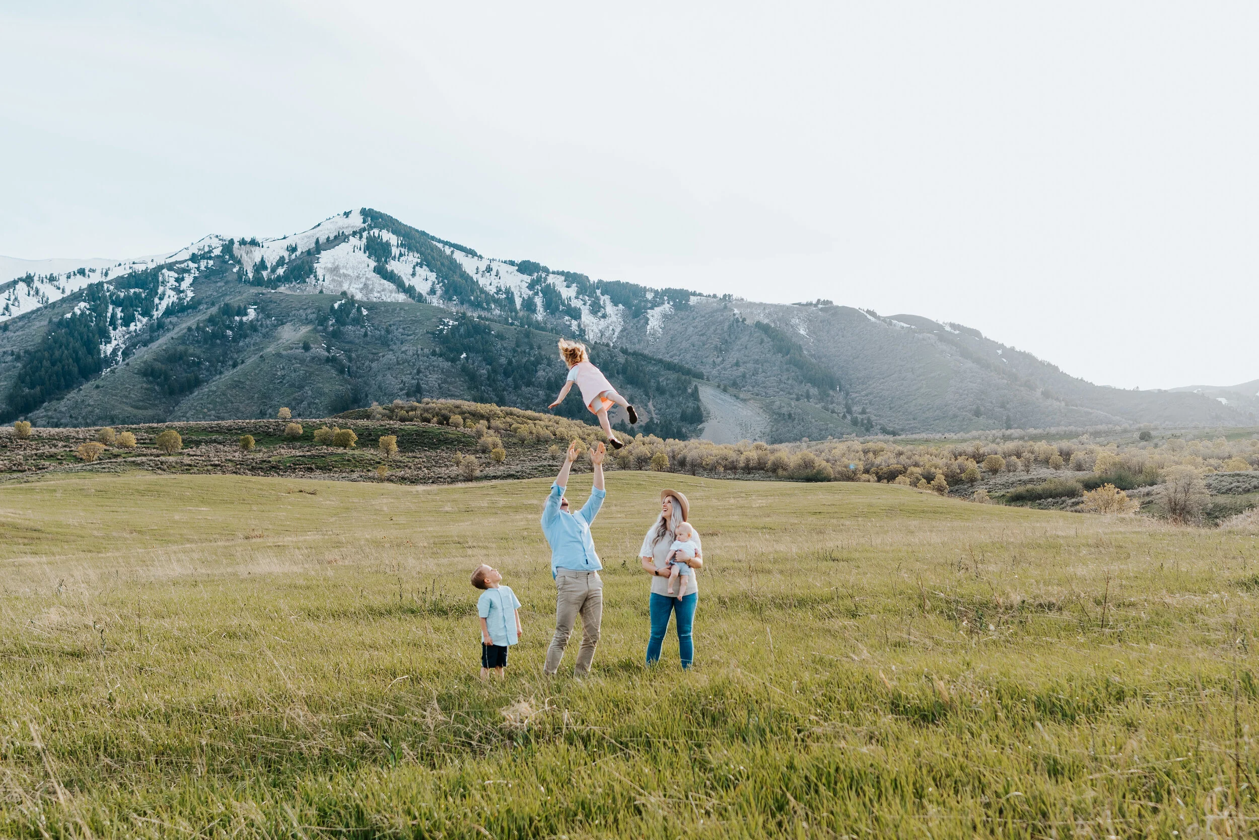 The Homer family poses as a group in the Wellsville Utah mountains for an unforgettable photoshoot. Dad throwing daughter for memorable family photoshoot funny family photo ideas Utah photography Logan Utah photographer Utah family photography Krist…