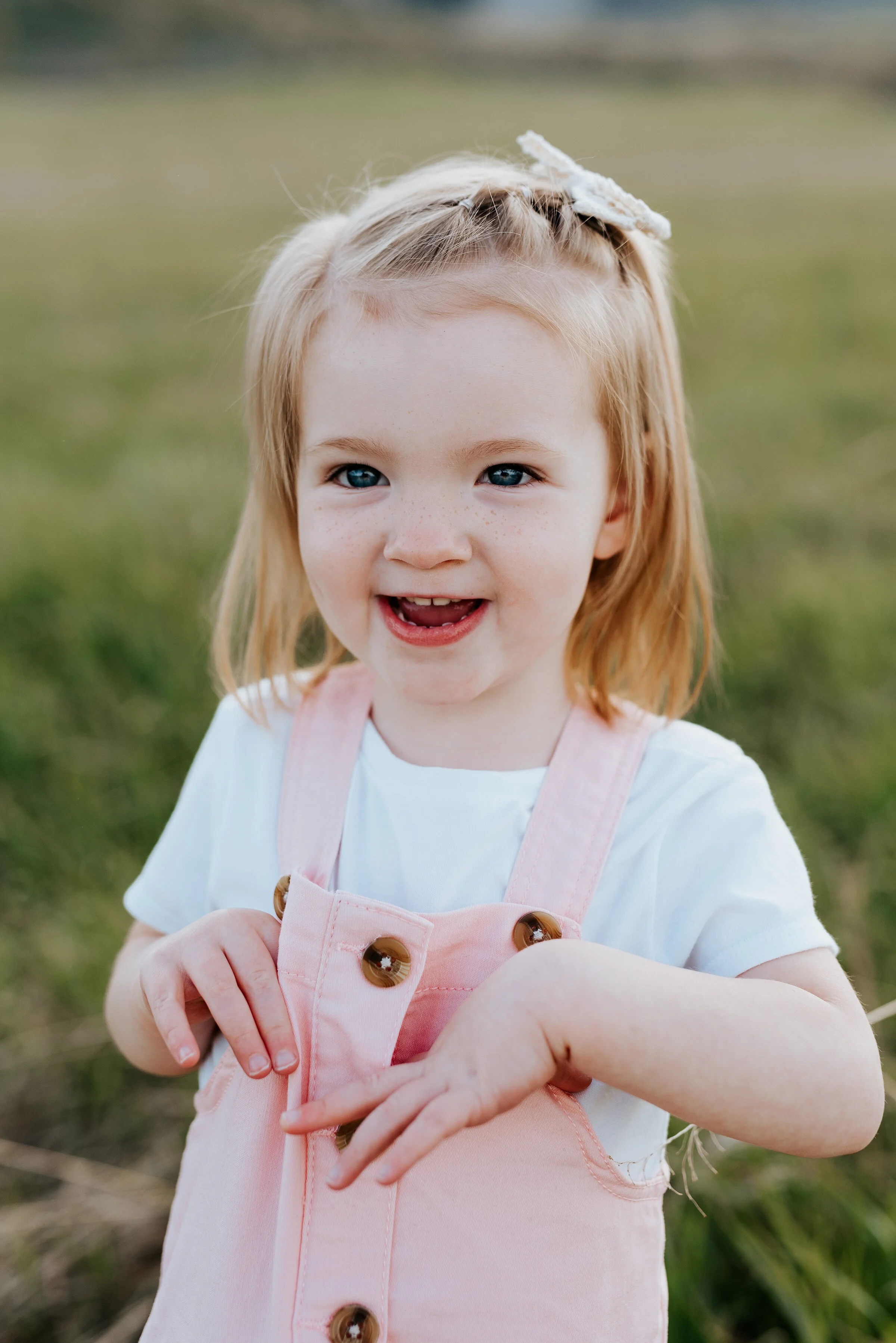  Adorable little girl's smile is captured during a family photoshoot in Logan Utah. Keepsake photography ideas childhood photos pink overalls family outfit ideas child poses for family photos candid family photos utah based photographer #utahfamilyph