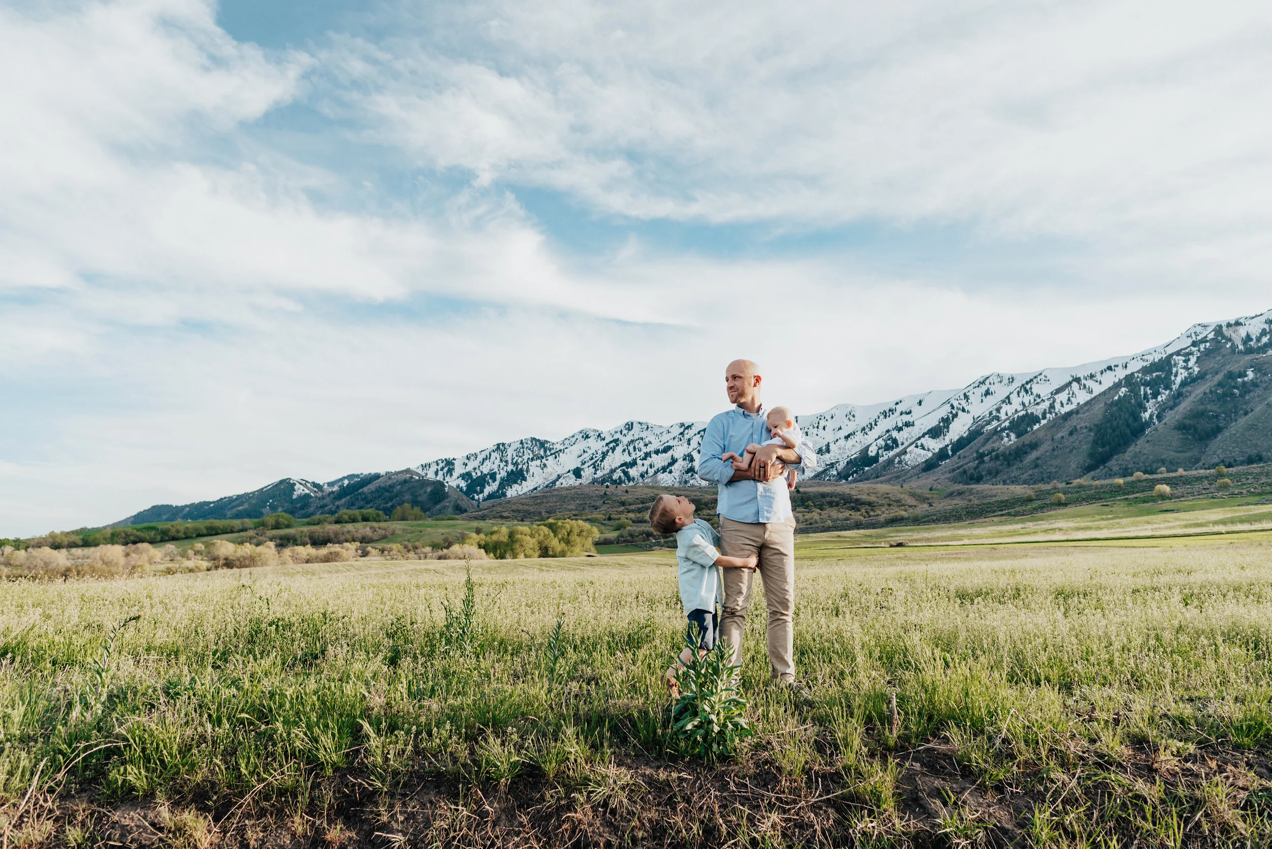 Dad holds his child with his other two children surrounding him while he looks hopeful into the distance. Logan utah photography kristi alyse photography daddy photoshoot father of the year portraits mountain family pictures cache valley photographe…