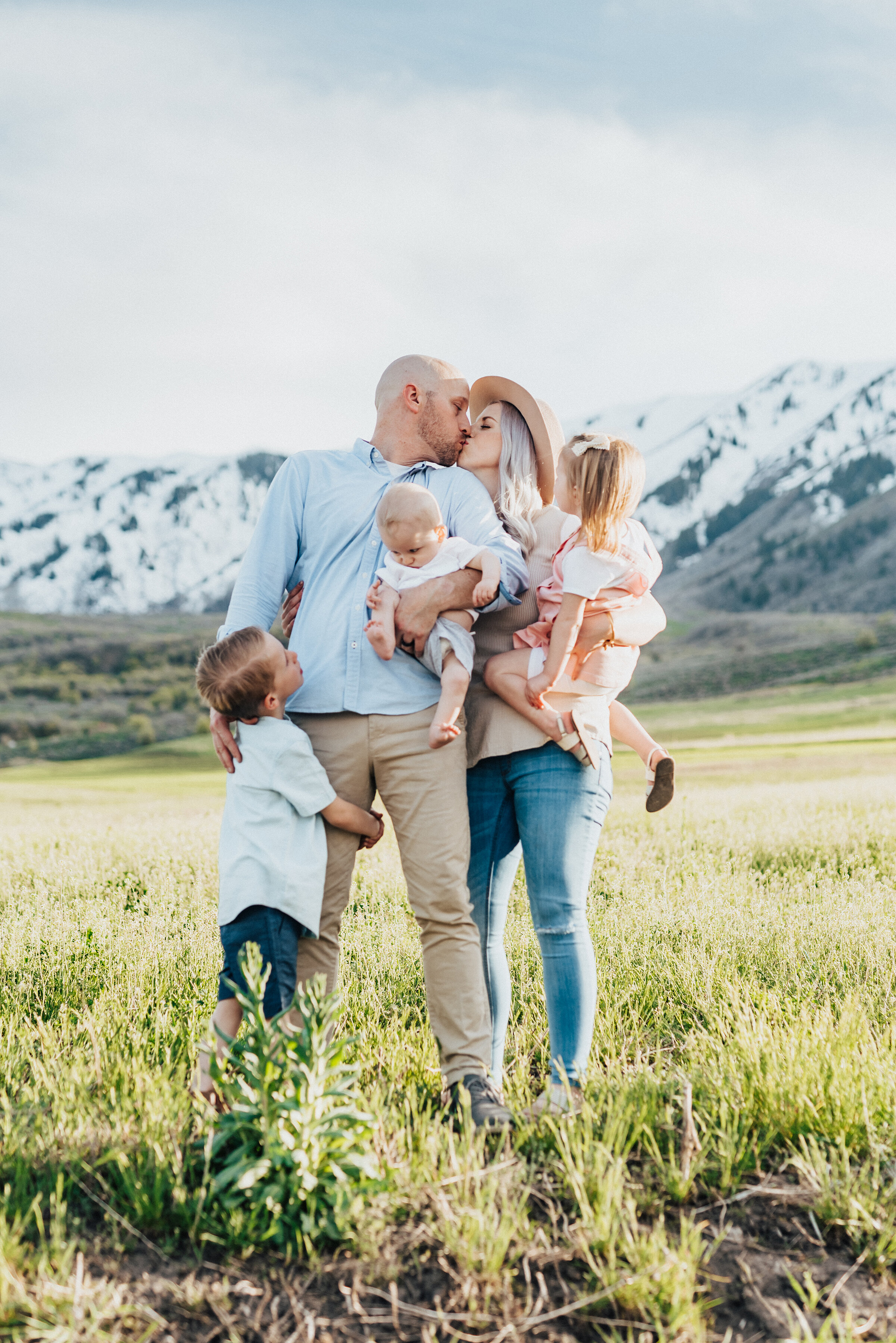 Mom and dad kiss while surrounded by their three children during a family photo session in logan utah. logan utah photography logan utah photographer mom of three children dad of three children family photography ideas family posing ideas family out