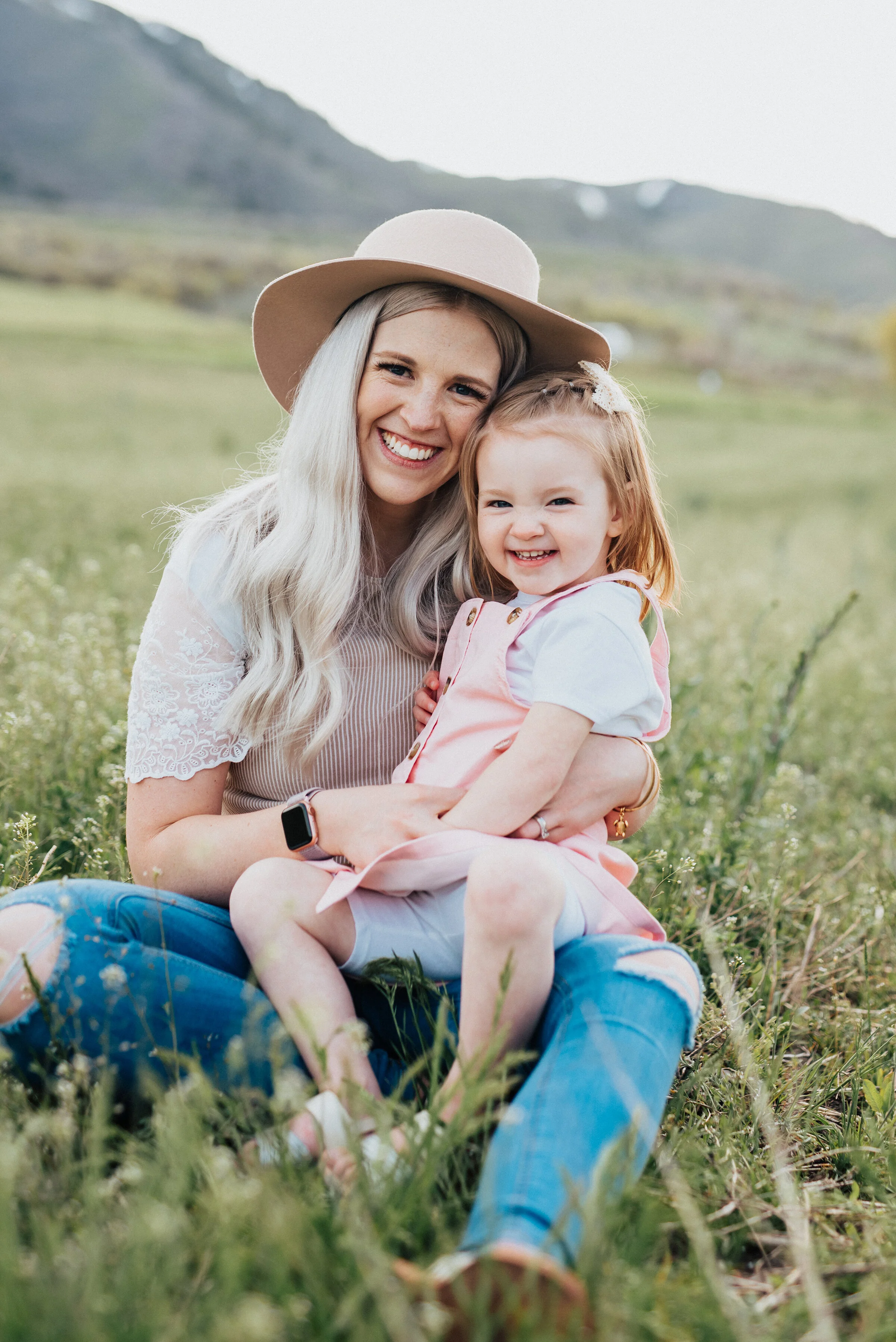  Mom smiles while holding daughter in the grass during a beautiful logan utah photography session with Kristi Alyse Photography. Mom ofgirls photo inspiration laughing photo ideas candid photography family portraits logan utah photographer laughter i
