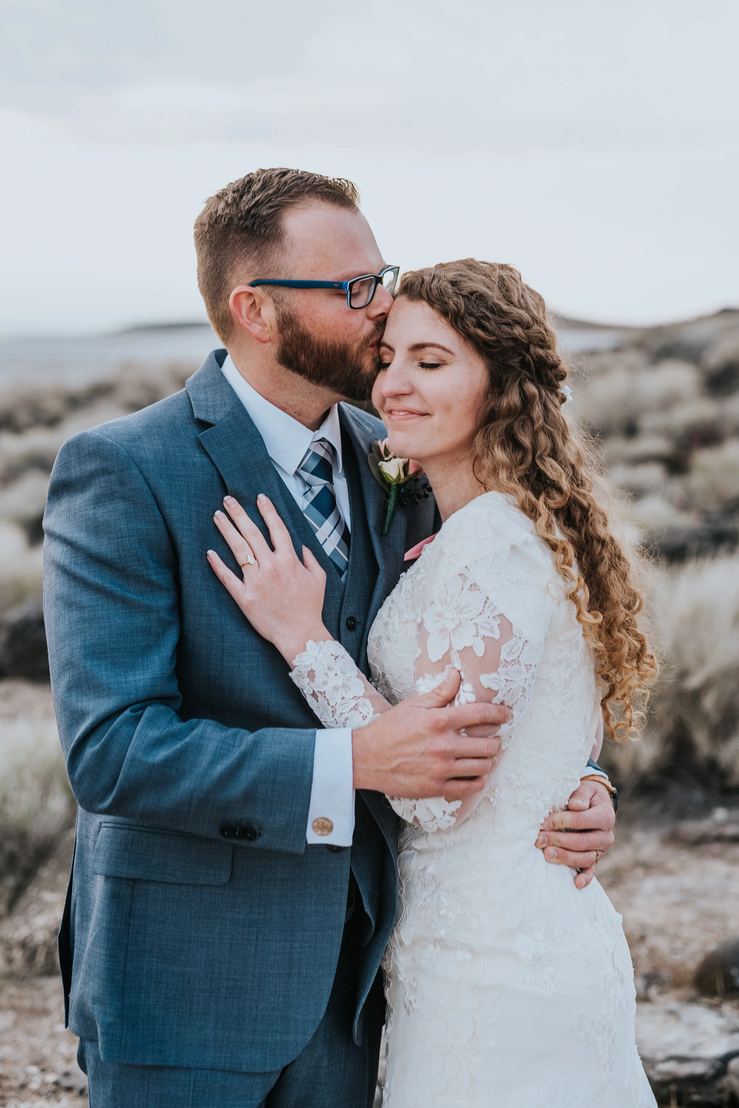  Bride and groom to be sharing a kiss on the forehead accenting her wedding band on one hand and their embrace. Wedding formal photoshoot in Spiral Jetty Northern Utah Great Salt Lake photography wedding formals natural photo aesthetic bride and groo