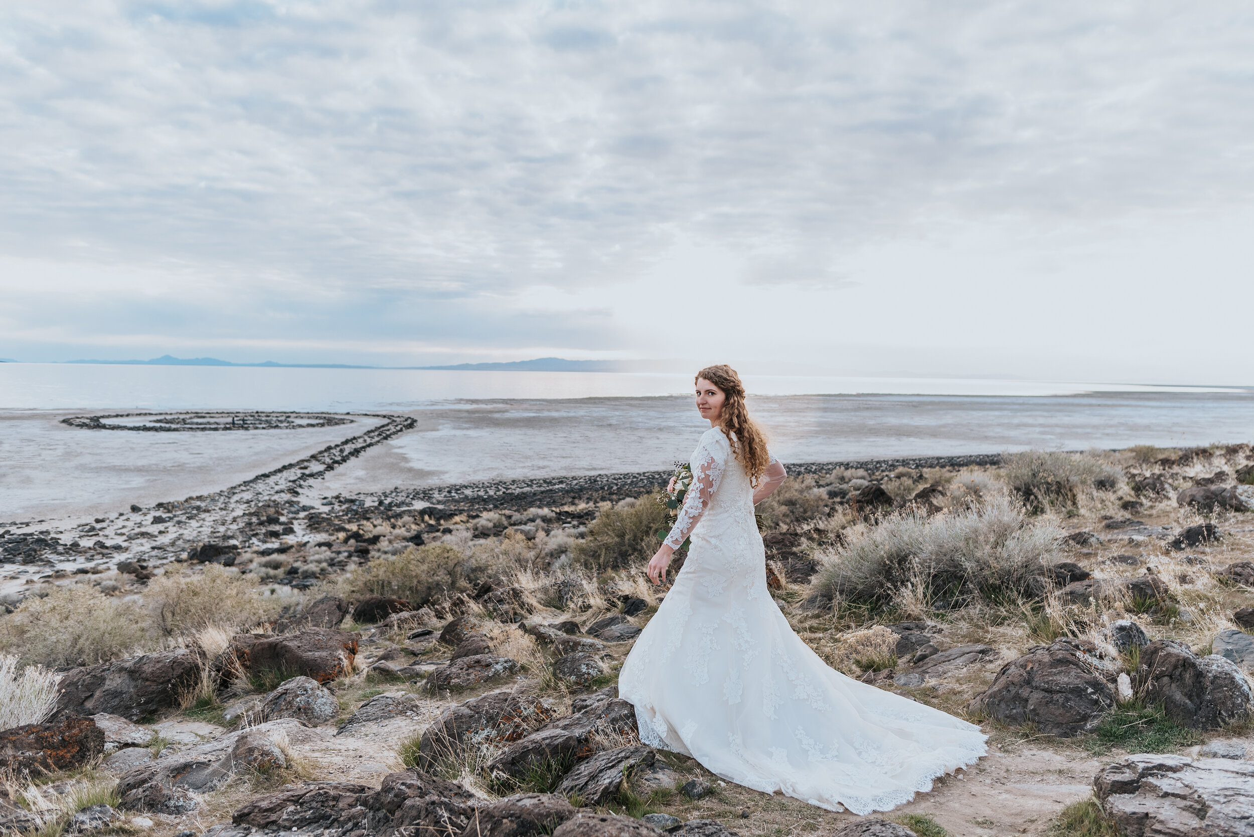  The full wedding gown and train for this bride was covered in lace from her shoulders down to the very end of her train that rushed over the rocks of the Spiral Jetty. Wedding formal photoshoot in Spiral Jetty Northern Utah Great Salt Lake photography wedding formals natural photo aesthetic bride and groom #spiraljetty #utahphotography #weddingformals #gettingmarried #weddingattire #utahwedding #greatoutdoorswedding #weddingformalsphotoshoot #naturalbeauty 