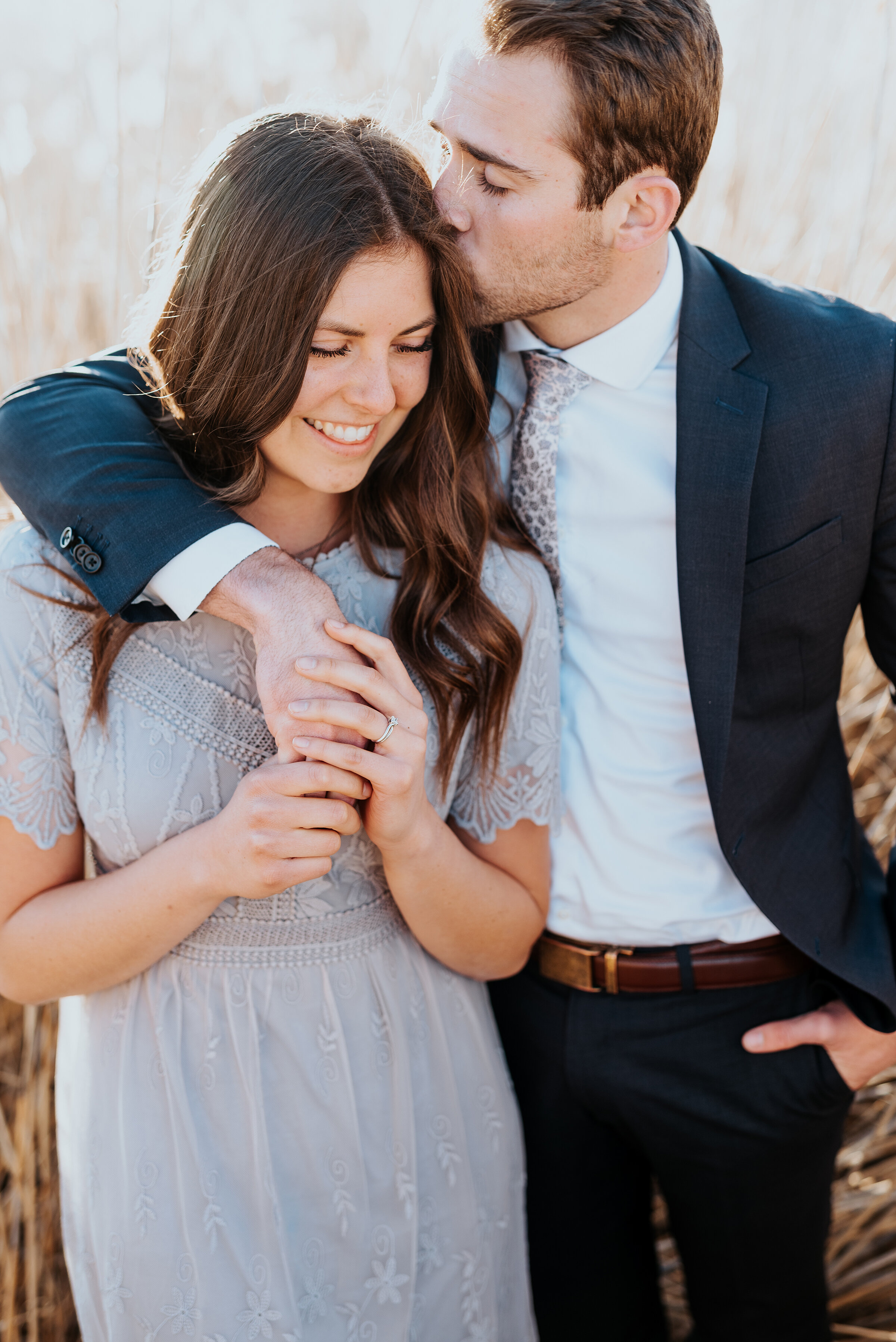  Man kisses his fiancé' head while she looks stunning in a gray lace dress during their engagement photoshoot. Kissing couple during their engagement photoshoot magna utah gray aesthetic outdoor photoshoot Kristi Alyse photography best utah photograp