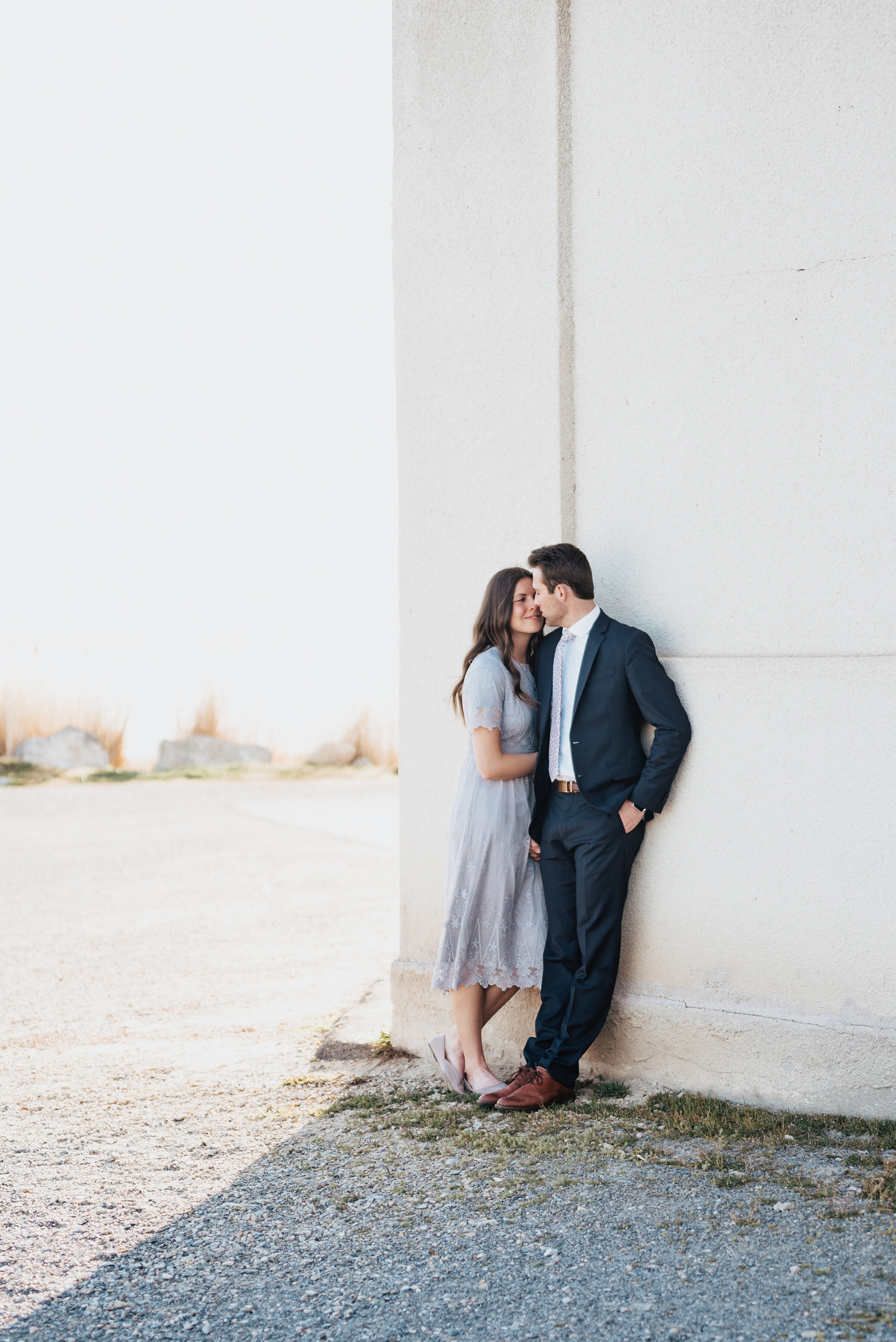  Couple poses in front of a large textured building in matching gray attire during their utah engagement photoshoot. Utah photoshoot utah engagement session priceless unforgettable engagement photos gray lace dress matching outfits for engagement sho
