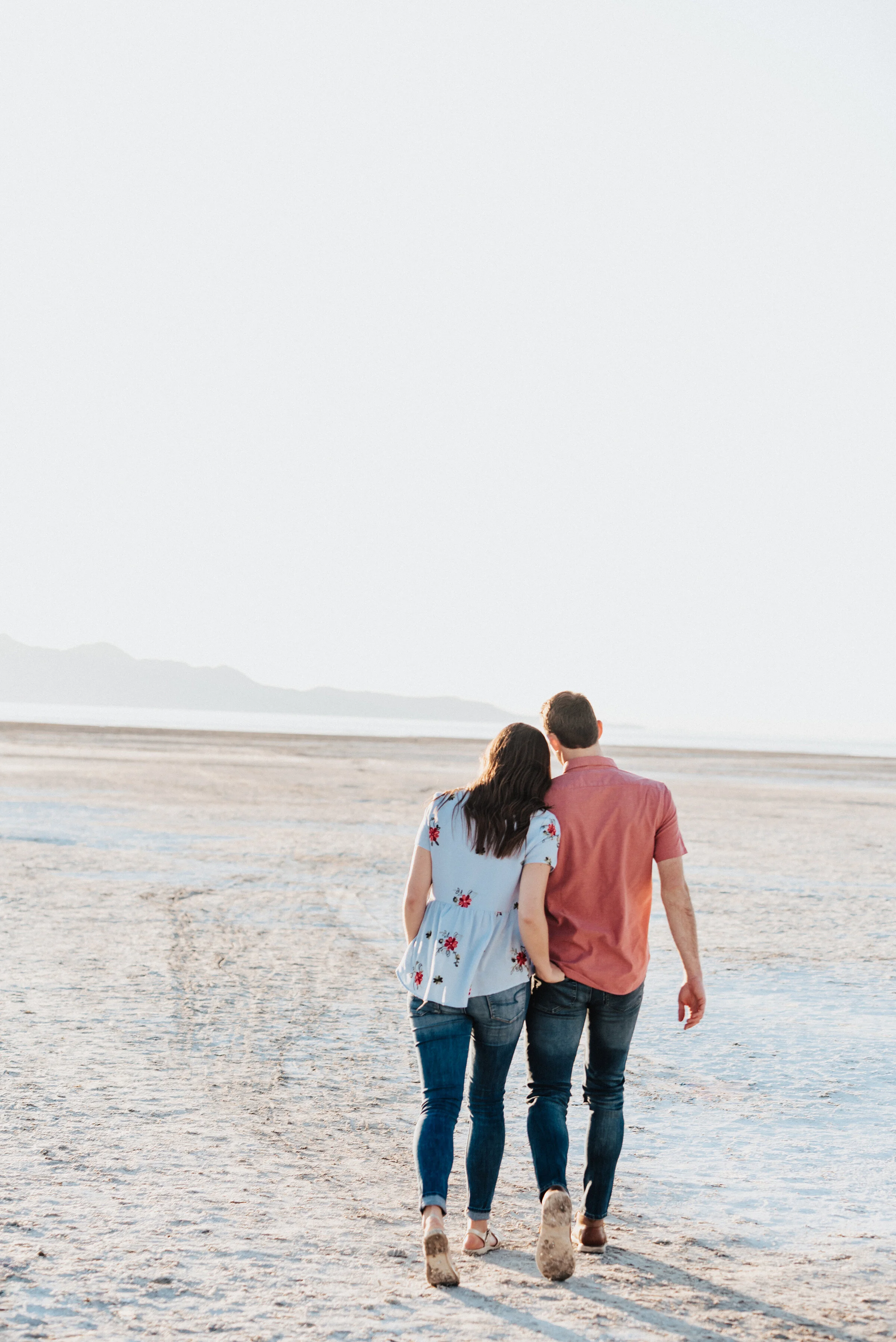  Couple looks across the salt flats in magna utah during their engagement photoshoot with Kristi Alyse Photography. Dry lake bed aesthetic magna utah photo locations outdoor nature engagement inspiration teal and coral matching outfits #kristialyseph
