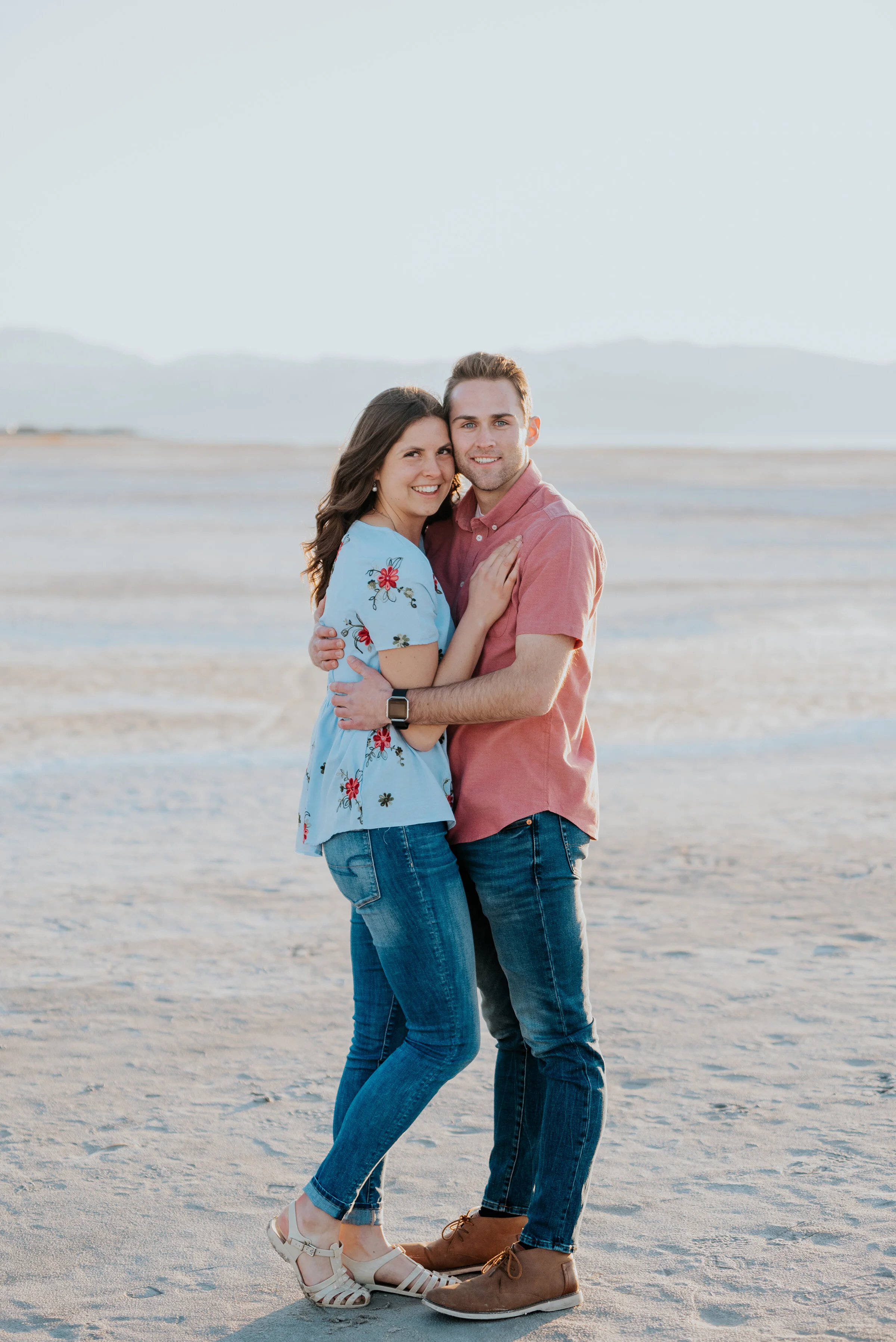  Couple looks across the salt flats in magna utah during their engagement photoshoot with Kristi Alyse Photography. Dry lake bed aesthetic magna utah photo locations outdoor nature engagement inspiration teal and coral matching outfits #kristialyseph