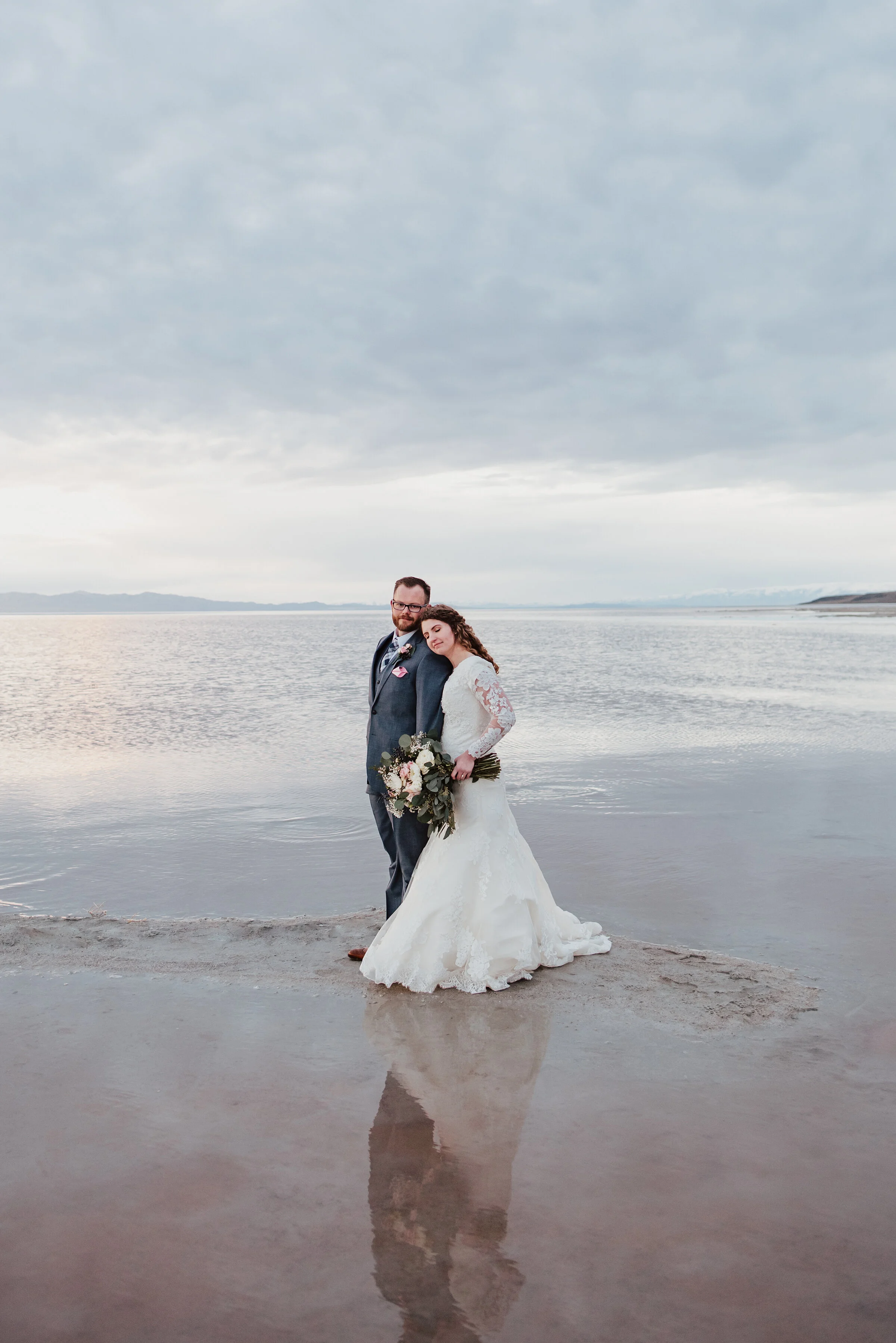  Enjoying the simple moments during their wedding formal photography session by walking down the sand as the sunset reflected off the water just beyond them. Wedding formal photoshoot in Spiral Jetty Northern Utah Great Salt Lake photography wedding 