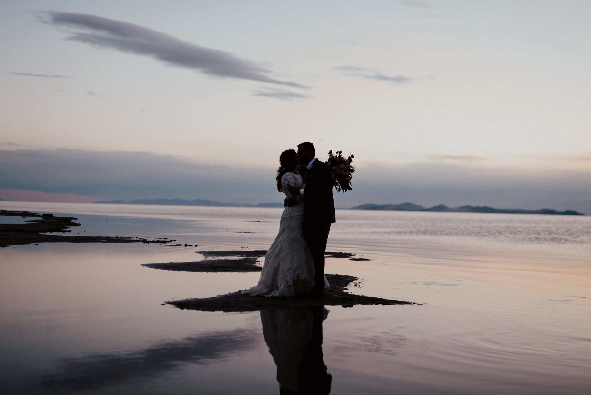 The sun had almost completely set on this bride and groom during their wedding formal session when one last kiss was needed to seal the deal at the Spiral Jetty in northern Utah. Wedding formal photoshoot in Spiral Jetty Northern Utah Great Salt Lake photography wedding formals natural photo aesthetic bride and groom #spiraljetty #utahphotography #weddingformals #gettingmarried #weddingattire #utahwedding #greatoutdoorswedding #weddingformalsphotoshoot #naturalbeauty