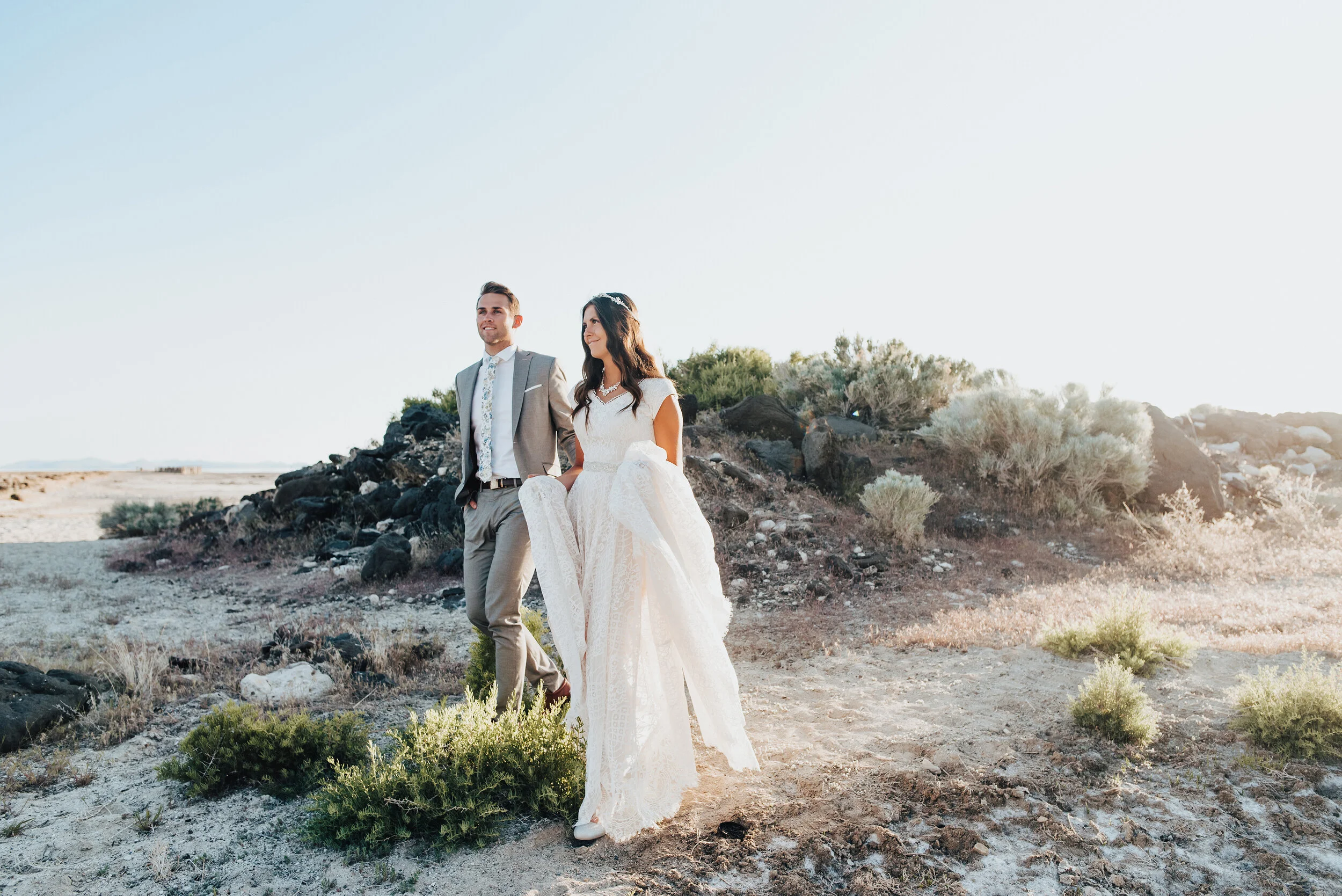 Walking down the rocky shore of the Great Salt Lake during a magical sunset formal session with this stunning bride and groom. Her lace wedding gown captured the lighting of the sunset in all the best ways and his grey suit was was made for this loc…