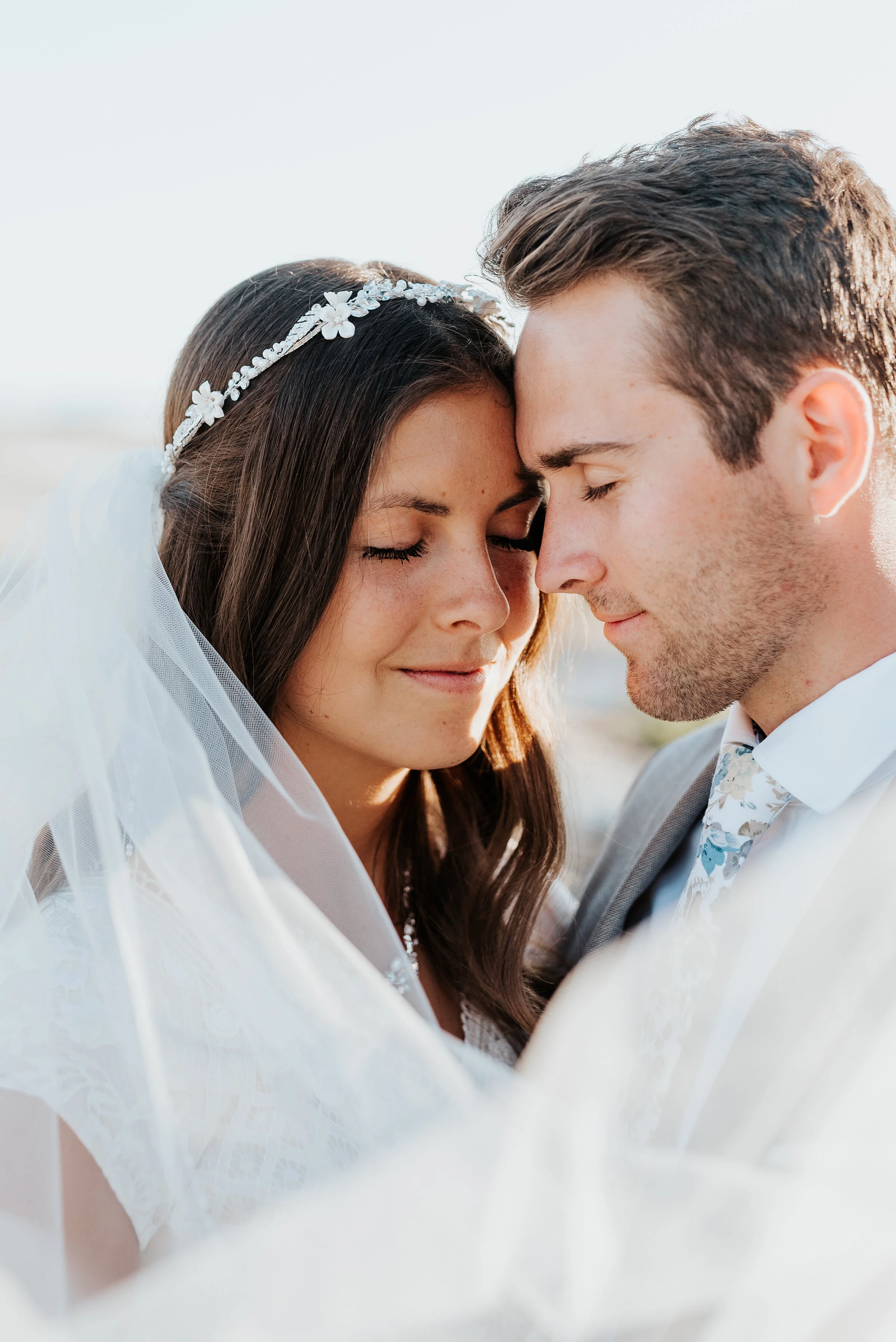  The bride and groom with their foreheads close together smiling with their upcoming wedding just around the corner. halo beaded headband long cathedral veil great salt lake formal session sunset sunkissed faces #spiraljetty #GreatSaltLake #formalses