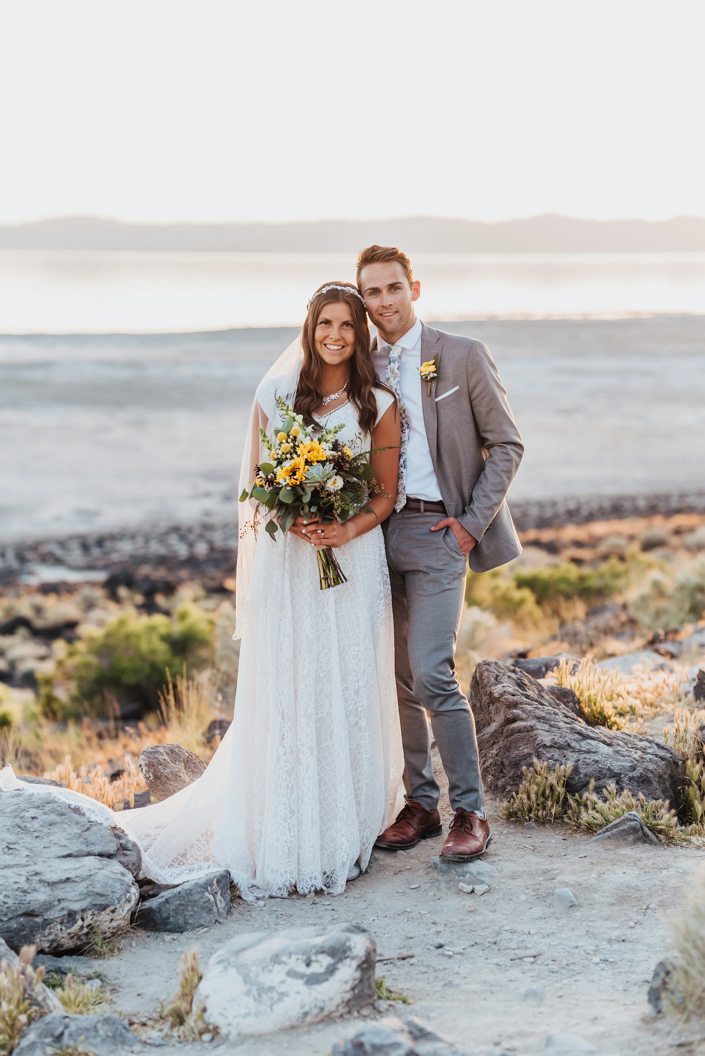  Smiling portrait photo of the bride and groom at the Great Salt Lake Spiral Jetty with bright yellow sunflowers in the brides bouquet. #spiraljetty #GreatSaltLake #formalsession #SaltFlats #sunsetphotosession #NorthernUtah #weddingphotographer #form