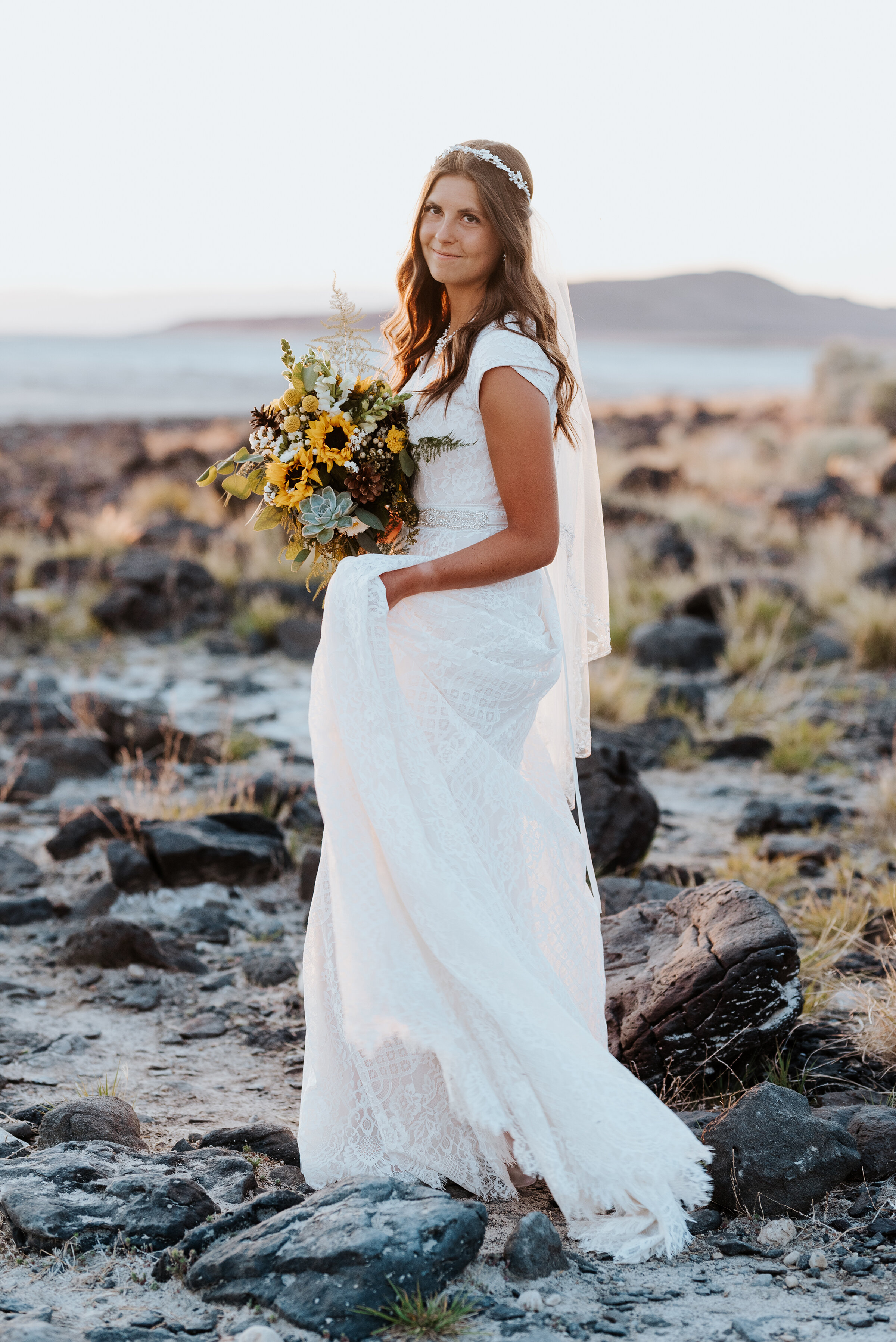  The stunning bride walking across the rocky Spiral Jetty shore with her sunflower bouquet and halo headband holding her gorgeous veil. #spiraljetty #GreatSaltLake #formalsession #SaltFlats #sunsetphotosession #NorthernUtah #weddingphotographer #form