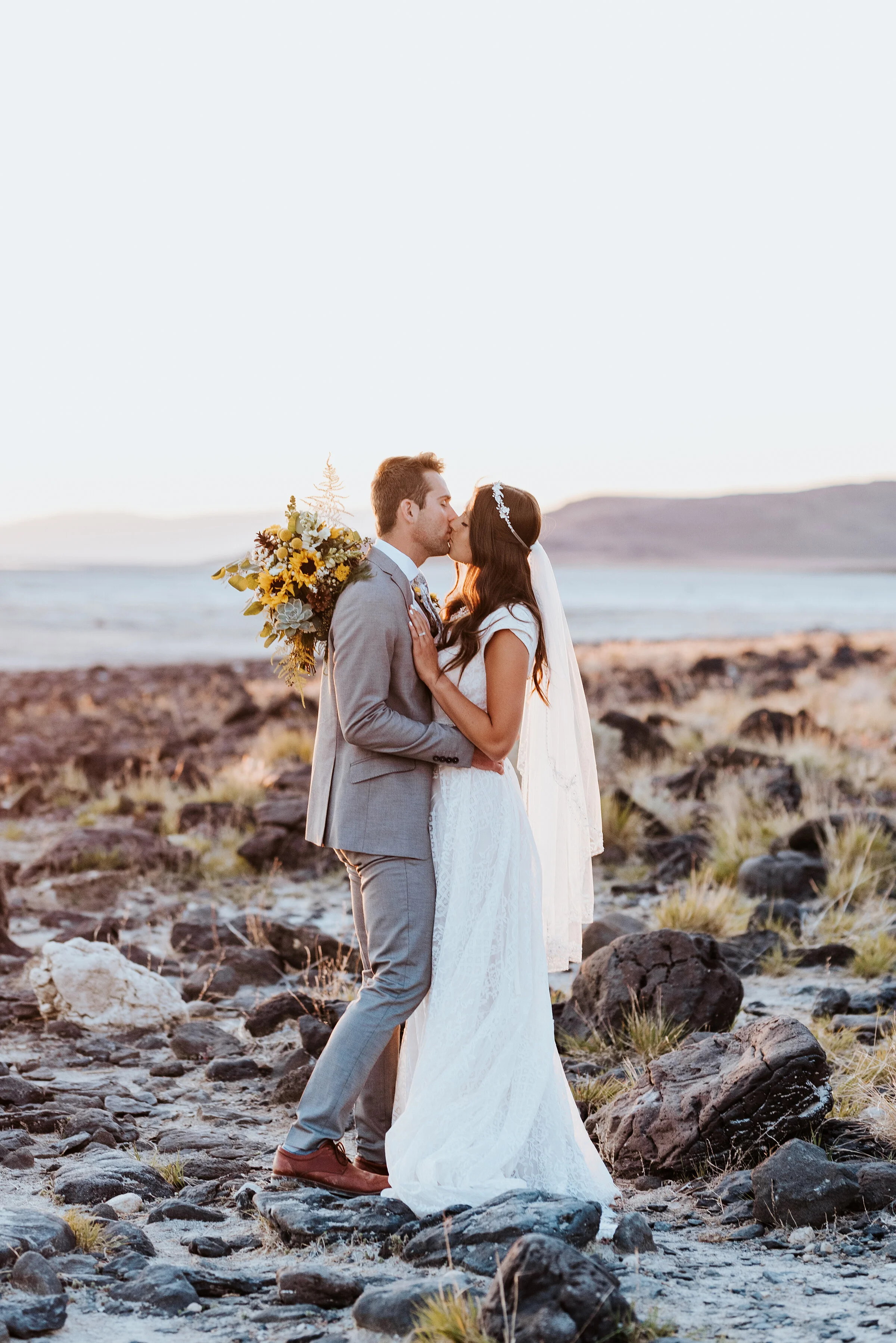  The bride and groom share a kiss just off the shore of the Great Salt Lake. The rocks provided texture to the background as the bride and groom captured the last of the sunshine rays in the distance. #spiraljetty #GreatSaltLake #formalsession #SaltF