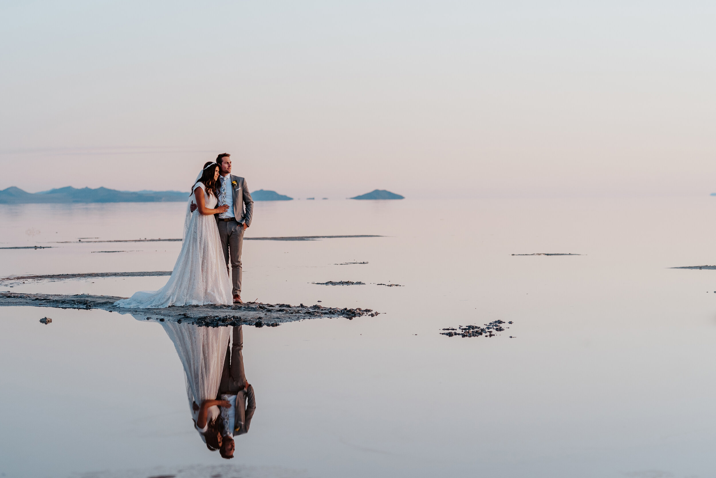  Arm in arm the bride and groom watched as the sun disappeared beyond the mountains  in the distance during their formal wedding photography session at the Spiral Jetty in Utah. #spiraljetty #GreatSaltLake #formalsession #SaltFlats #sunsetphotosessio