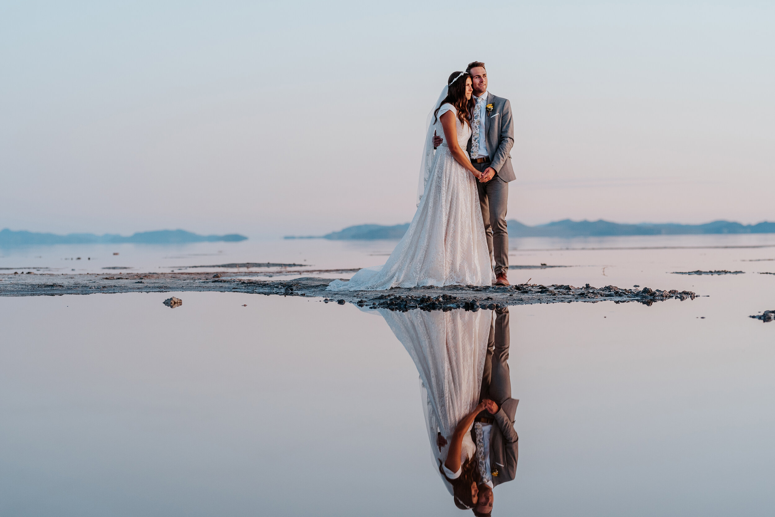 Stunning last moments of sunlight as the bride and groom stand together with their reflections in the water watching the sun disappear beyond the distant mountain ranges in Northern Utah. #spiraljetty #GreatSaltLake #formalsession #SaltFlats #sunset…