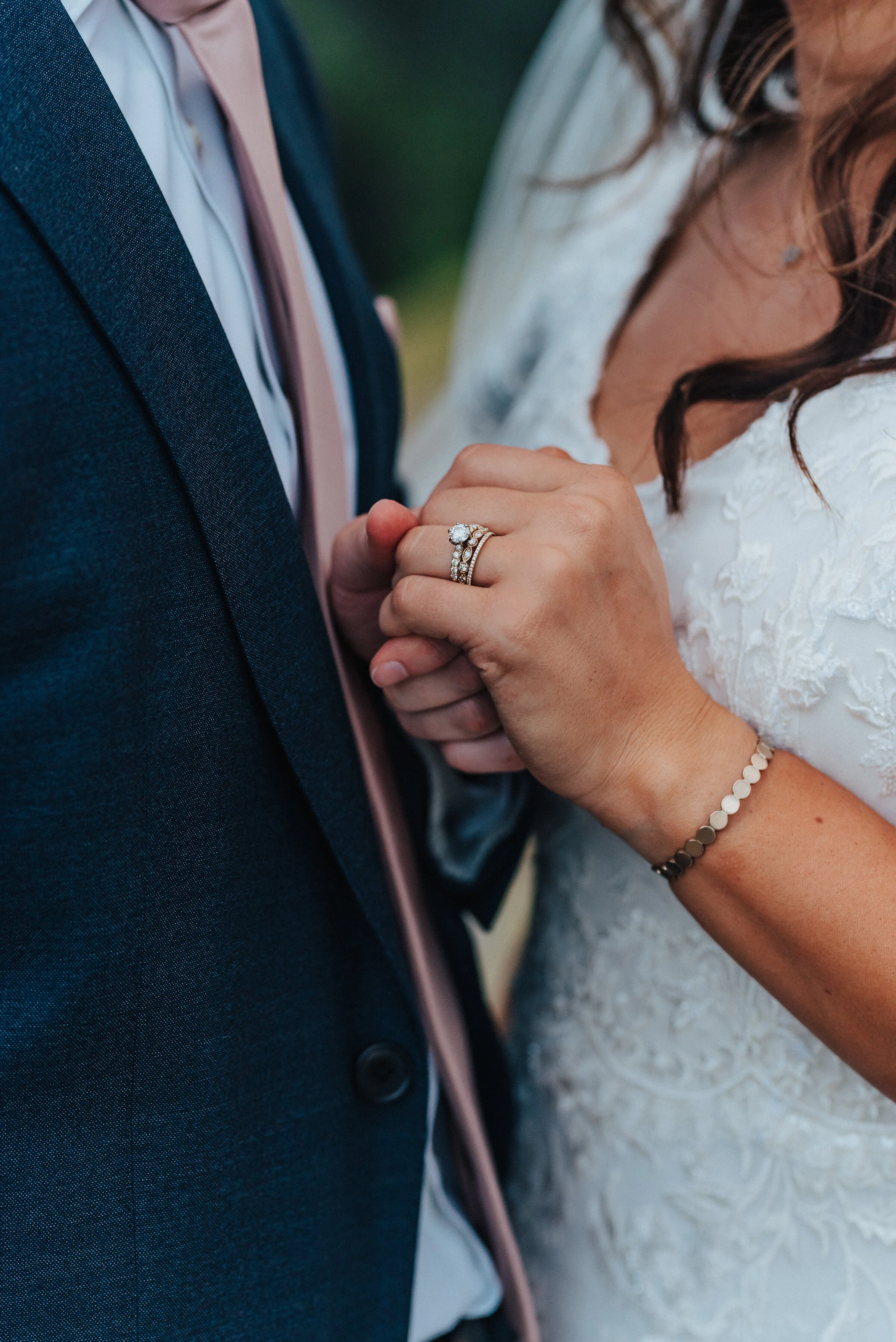  The bride’s hand and beautiful ring steal the focus of this photo as her husband gently grabs her hand. Almost interlocked hands navy blue suit and dress close-up in American Fork floral dress design gorgeous engagement ring #husbandandwife #younglo