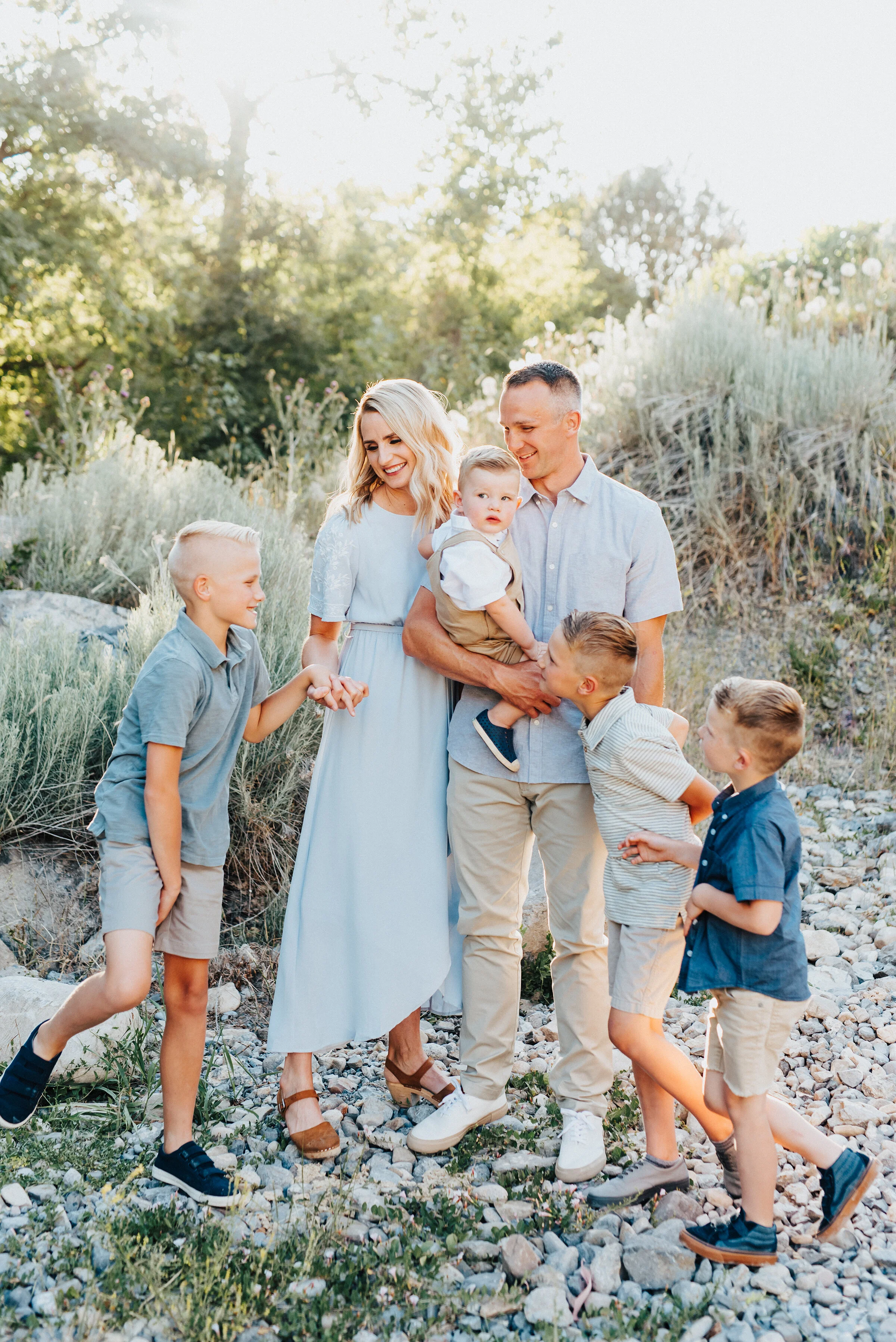  A beautiful family is holding hands while exchanging looks with each other on a sunlit hillside in Providence Canyon, UT. Light blue and khakis soft outdoor setting family photoshoot looking at different directions backlit sunlight utah dessert  #pr