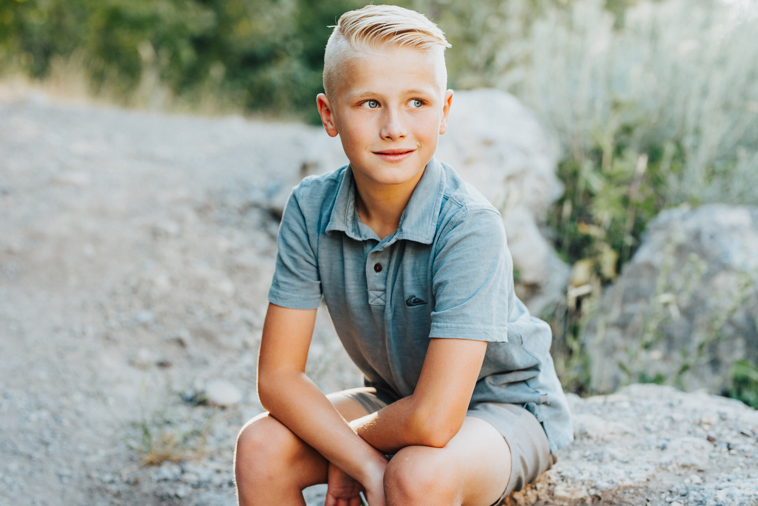A handsome blue-eyed boy looks off into the distance while sitting casually on a rock in Providence Canyon, UT. Soft outdoor setting casual sitting blonde hair and blue eyes crossed arms sitting #providencecanyon #utahphotography #utah #familyphoto #family #familyphotography #familyphotographer #photography #love #familytime #familyphotoshoot #familyportrait #familyfirst #photooftheday