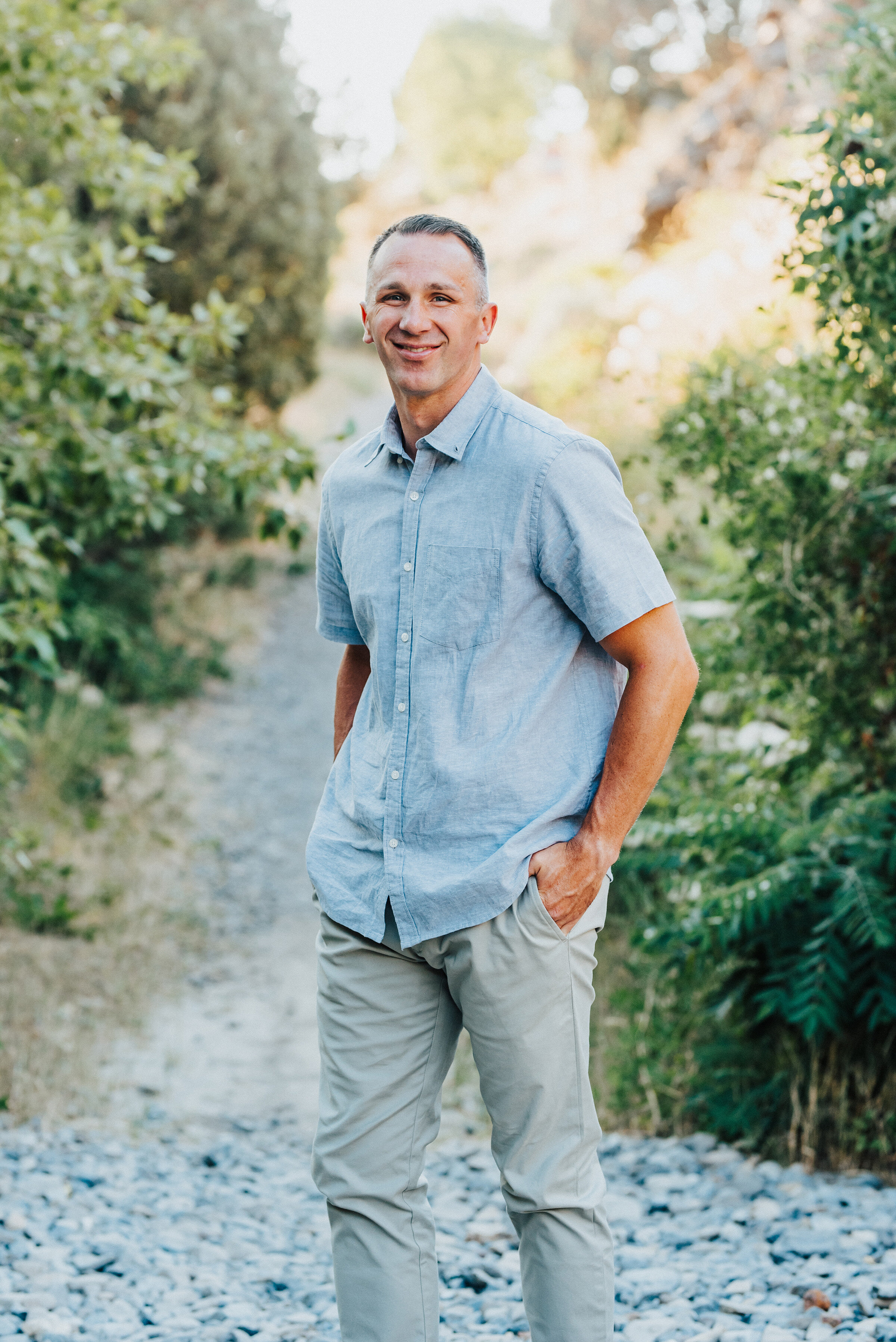  Handsome dad tucks his hands into his pockets and gives a subtle smile while on a stony path in the canyon. Light blue and khakis collected pose providence canyon utah standing alone #providencecanyon #utahphotography #utah #familyphoto #family #fam