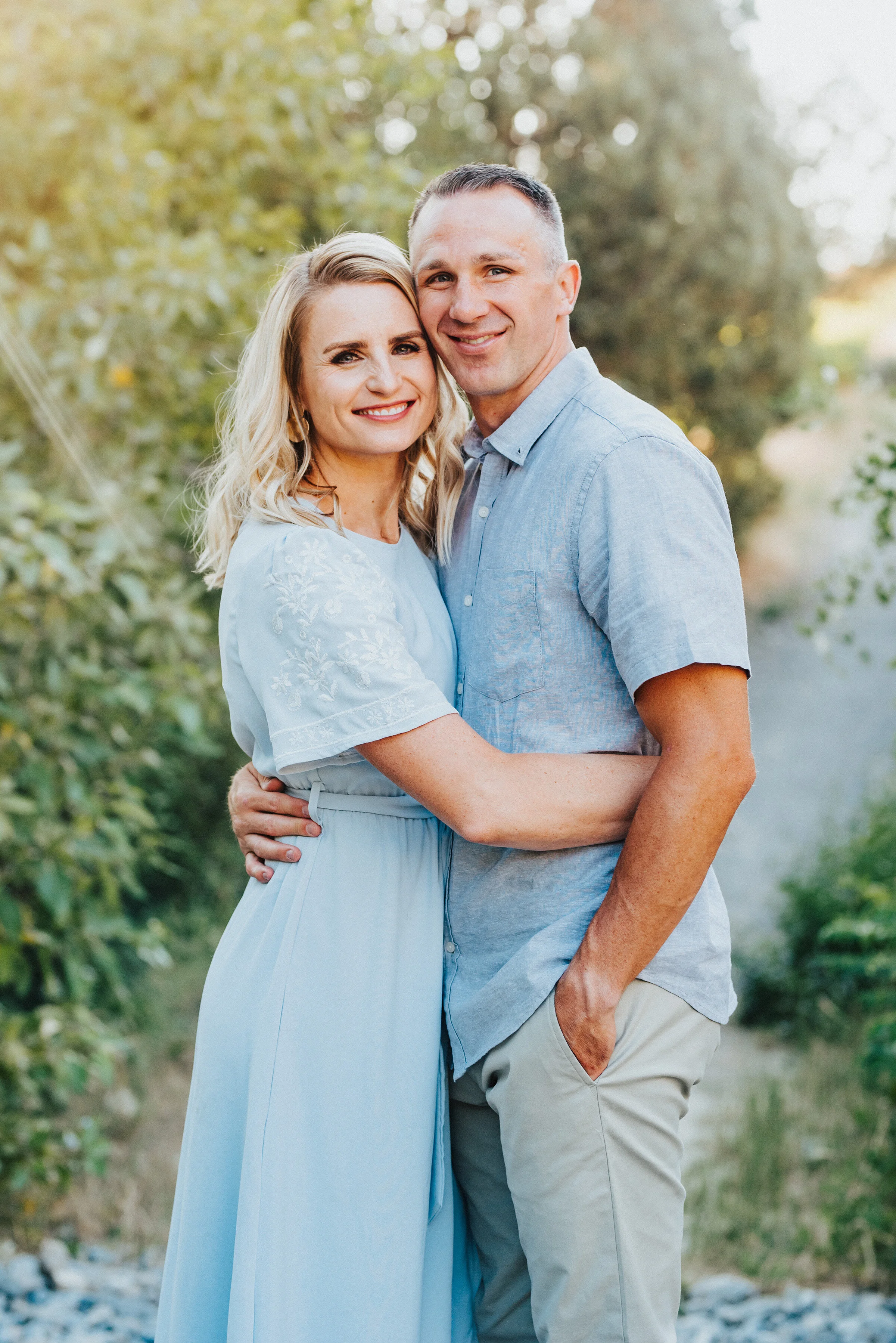  A gorgeous couple embrace each other while smiling toward the camera in their perfectly coordinated outfits. Light blue and khaki soft outdoor setting relaxed romantic pose providence canyon utah #providencecanyon #utahphotography #utah #familyphoto