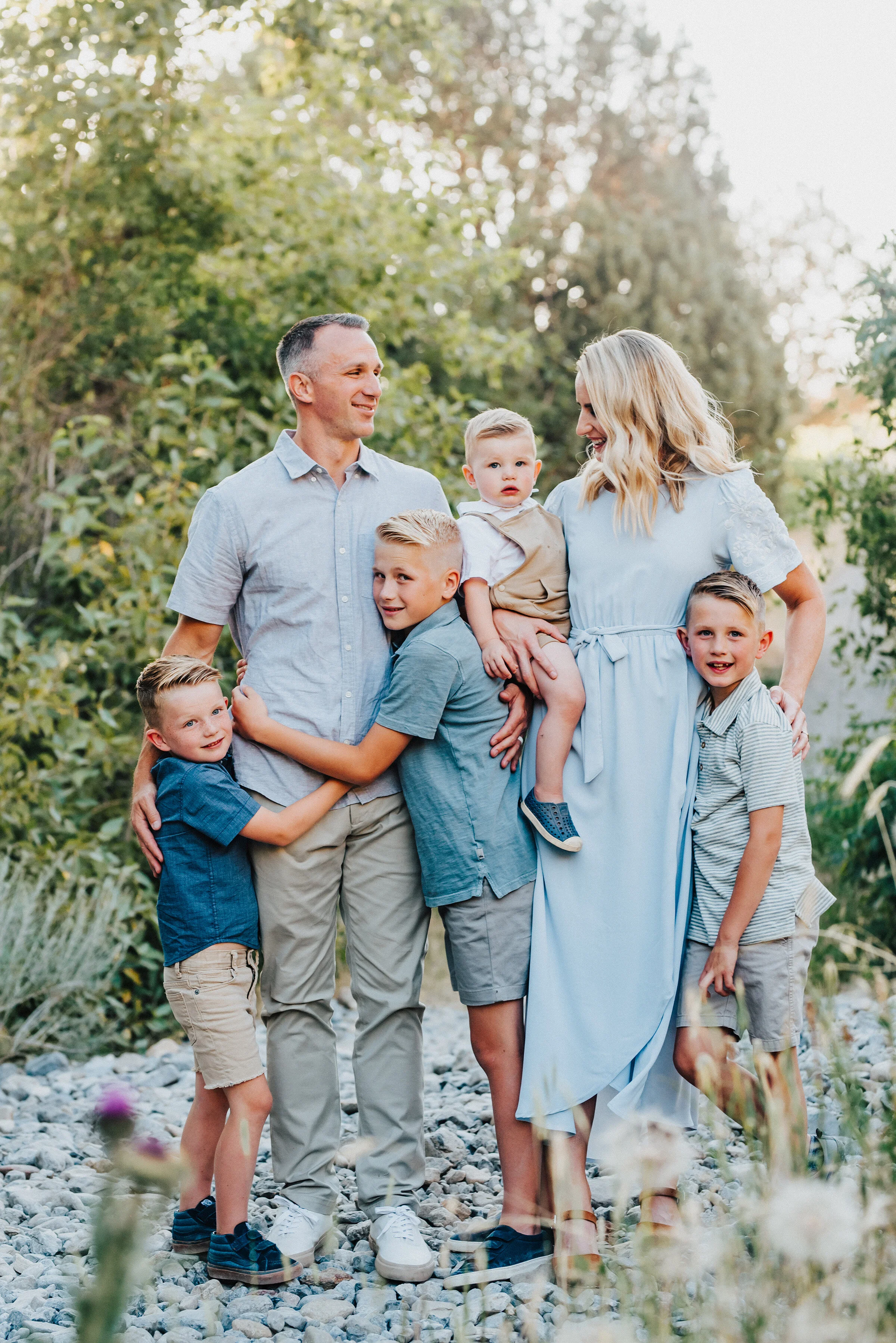  Gorgeous shot of a family embracing and looking at each other in the sunlit canyon on a stony pathway. Light blue and khakis soft outdoor setting looking at different directions family all together #providencecanyon #utahphotography #utah #familypho