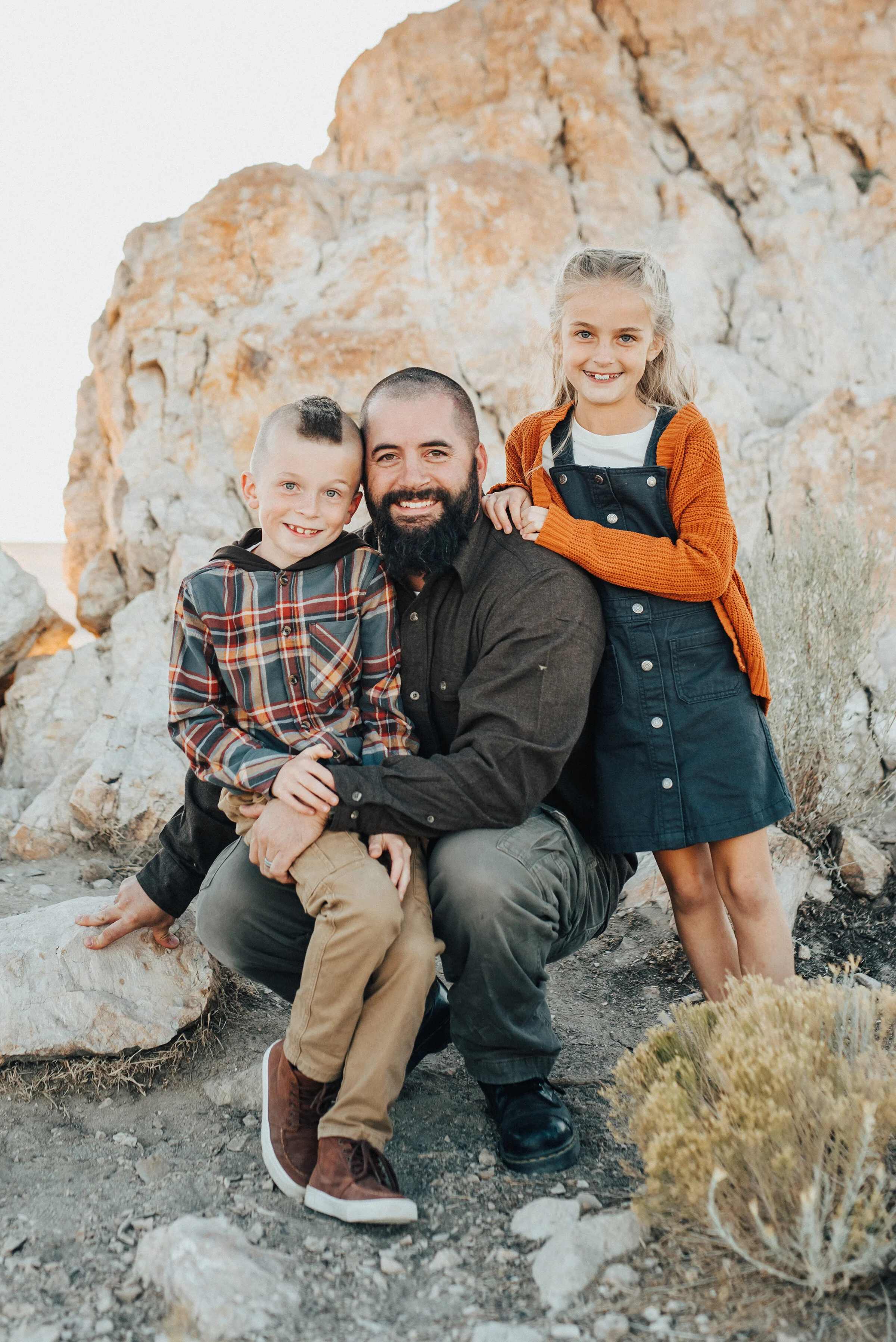  A darling father and his son and daughter sit together in the rocks of Antelope Island in a professional family photo shoot. Professional Utah photographer Kristi Alyse Photography father and his children outdoor fall outfit inspiration family goals