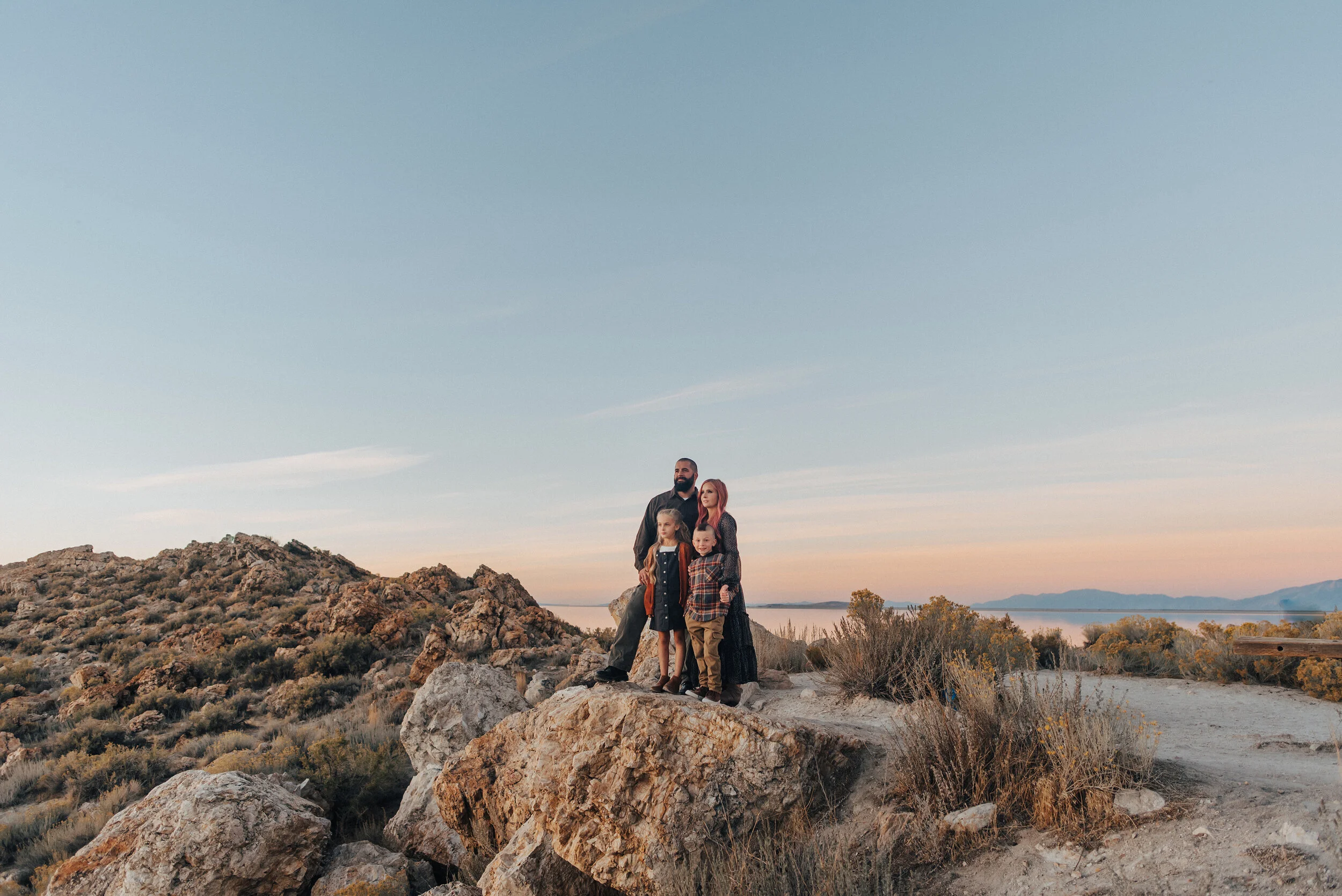 A stunning family stares into the distance in a beautiful sunset family photo shoot in Syracuse Utah’s Antelope Island. Family pose goals young family photo shoot inspiration family attire inspiration ideas and goals  pink hair goals professional Ut…