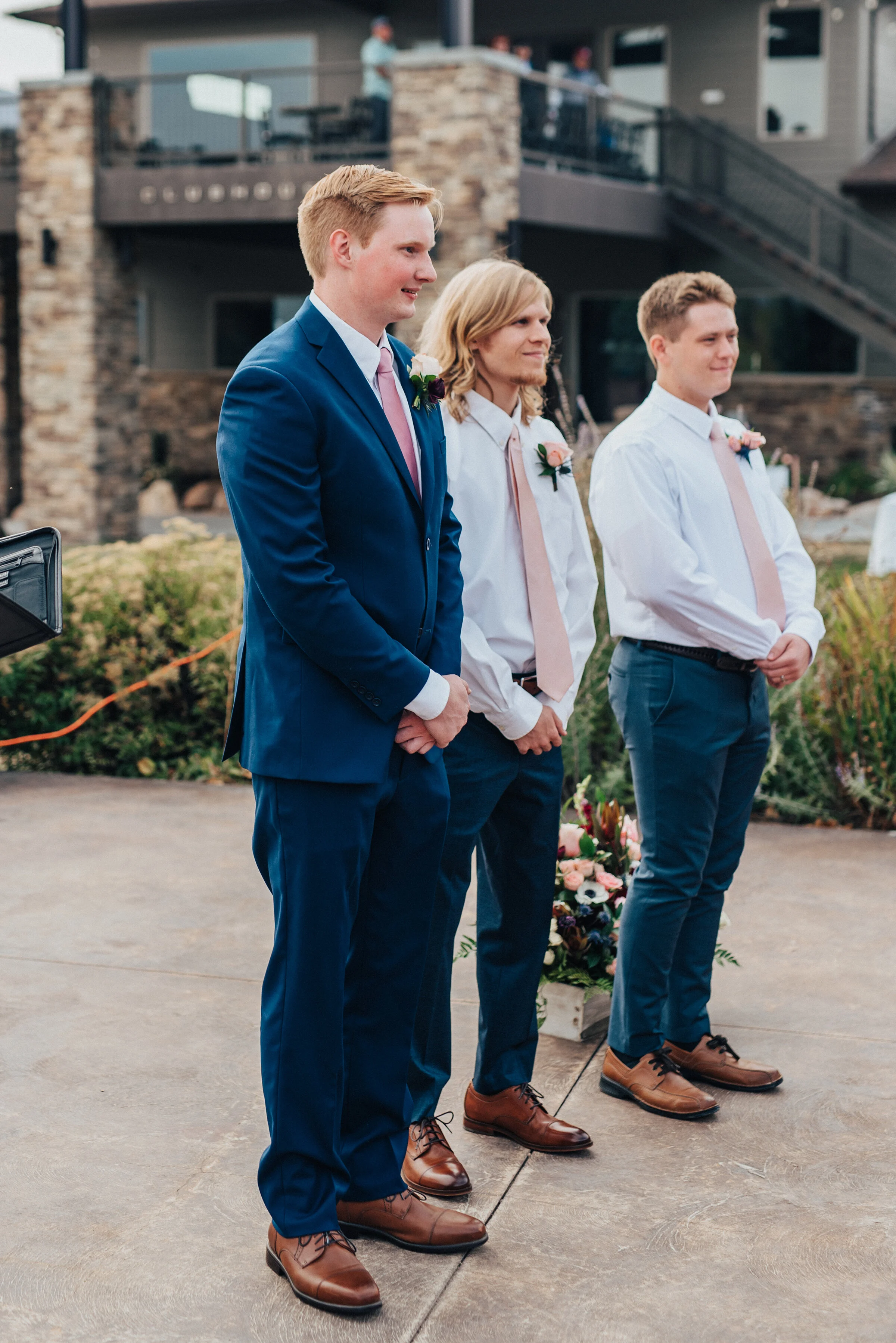  Handsome shot of the groom and groomsmen awaiting the ceremony in Logan, Utah captured by Kristi Alyse Photography. Groomsmen line wedding day blue suits pink tie wedding ceremony in northern Utah quality moments photography grooms boutonnieres best