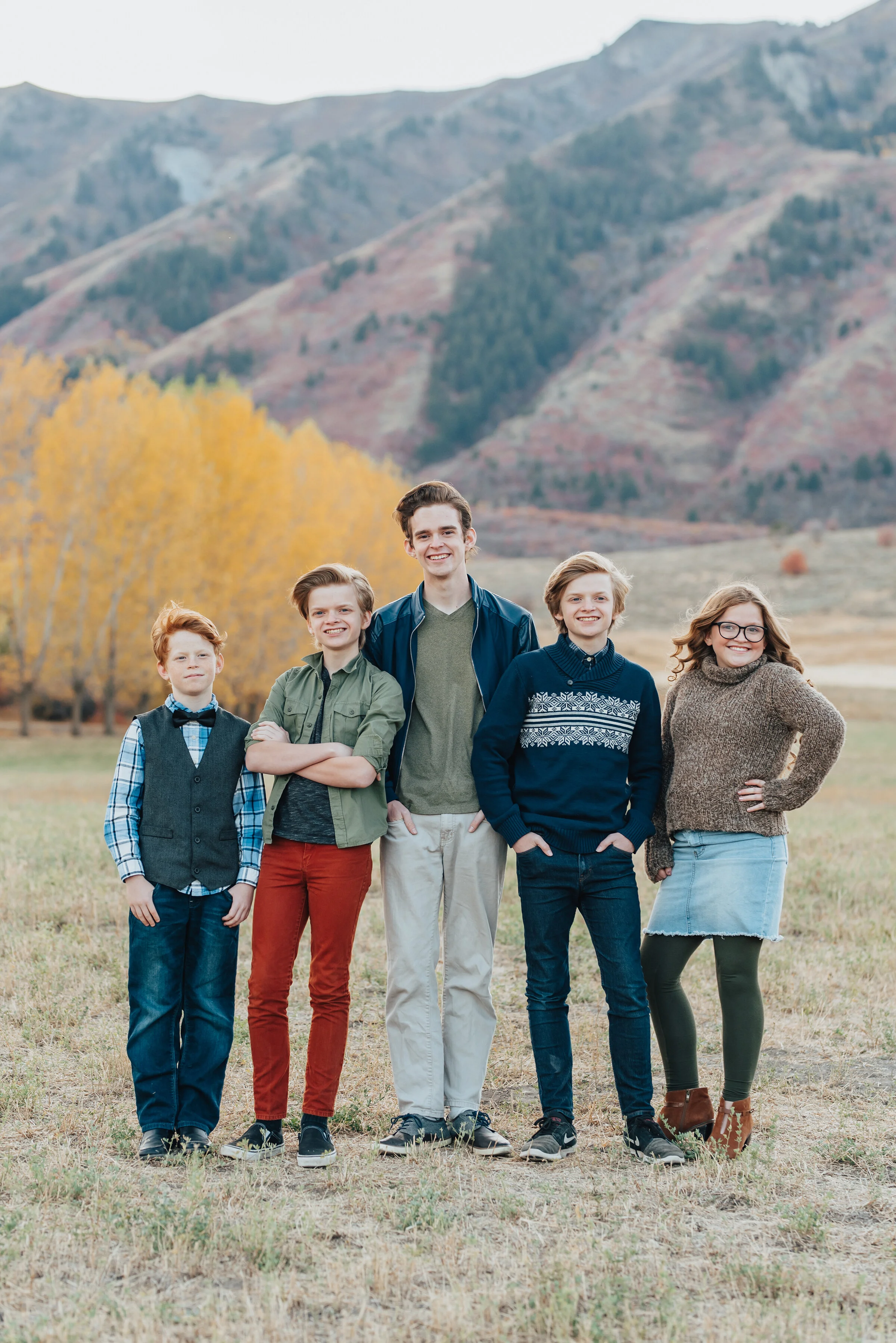  Outdoor family portrait series in Logan, Utah featuring the five children, four boys and one girl, smiling and posing, dressed in Fall colors with trees and mountains in the background, photographed by Kristi Alyse Photography. quality family photog