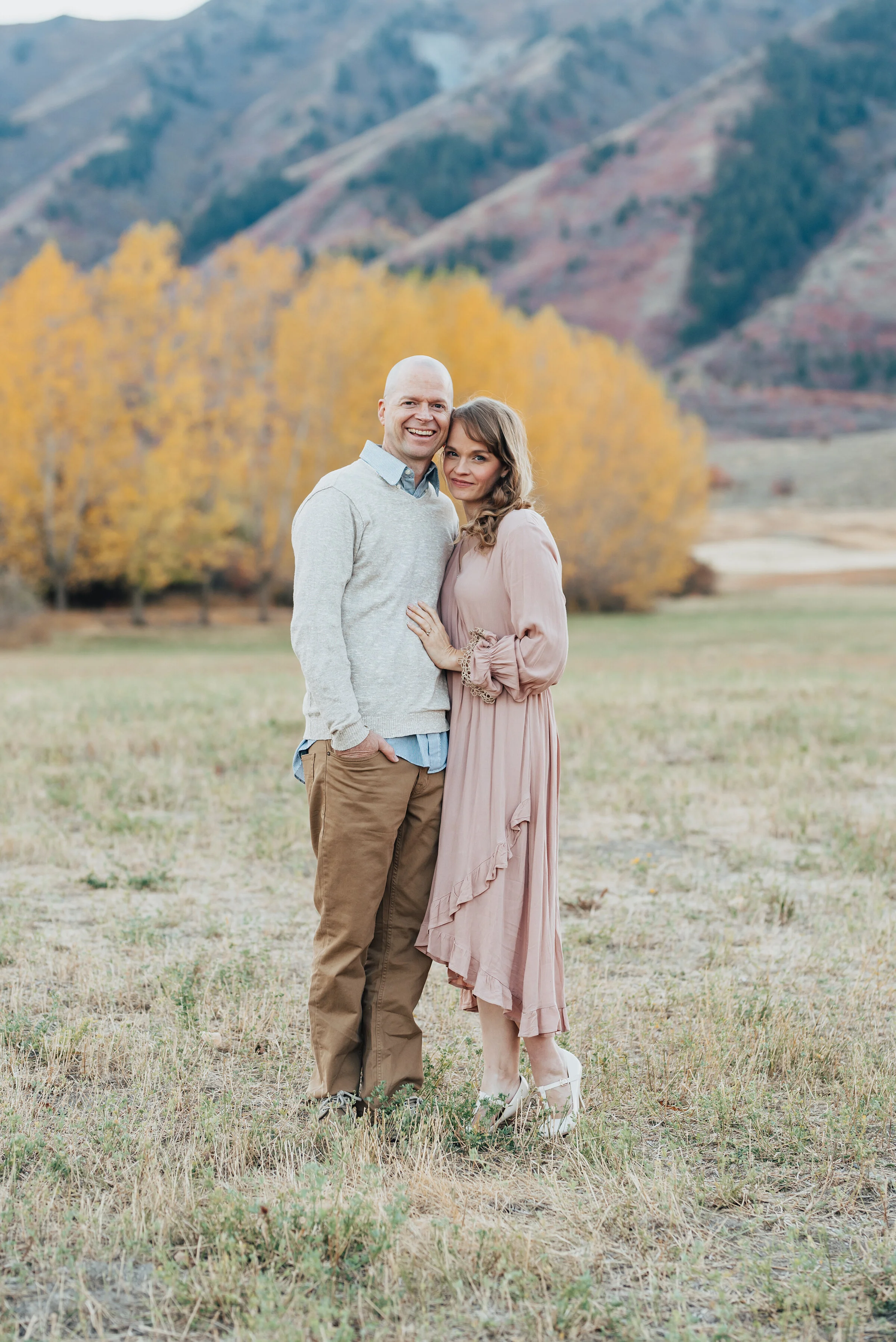  Outdoor family portrait featuring the dad and mom, posed and smiling at the camera, with yellow trees and mountains in the background, photographed by Kristi Alyse Photography. quality wedding photography family photography meaningful family photogr