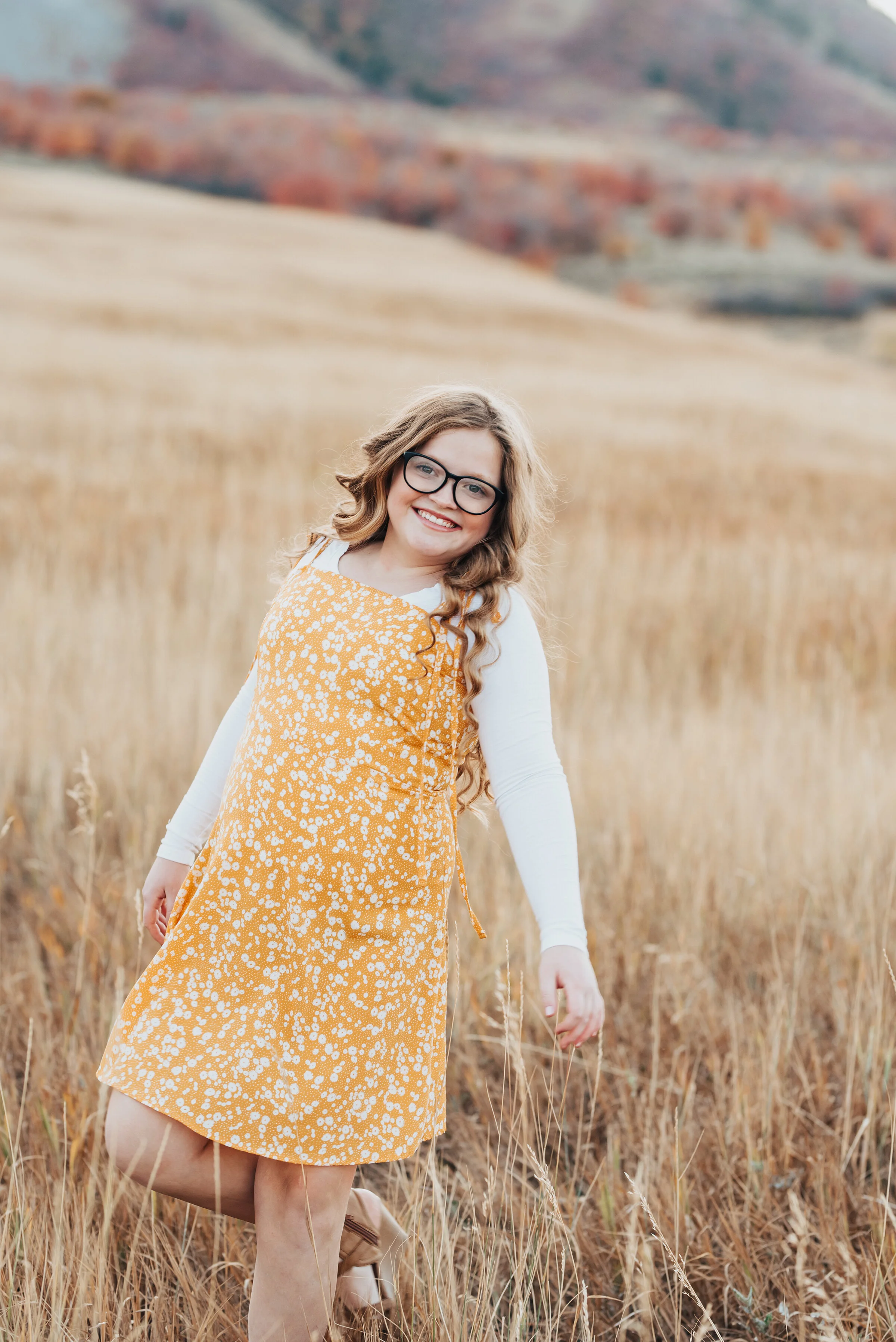  A portrait of a girl dressed in a golden yellow dress with cream print over a long sleeve cream shirt, standing in a field of wild grass, photographed by Kristi Alyse Photography. quality wedding and family photography meaningful family photography 
