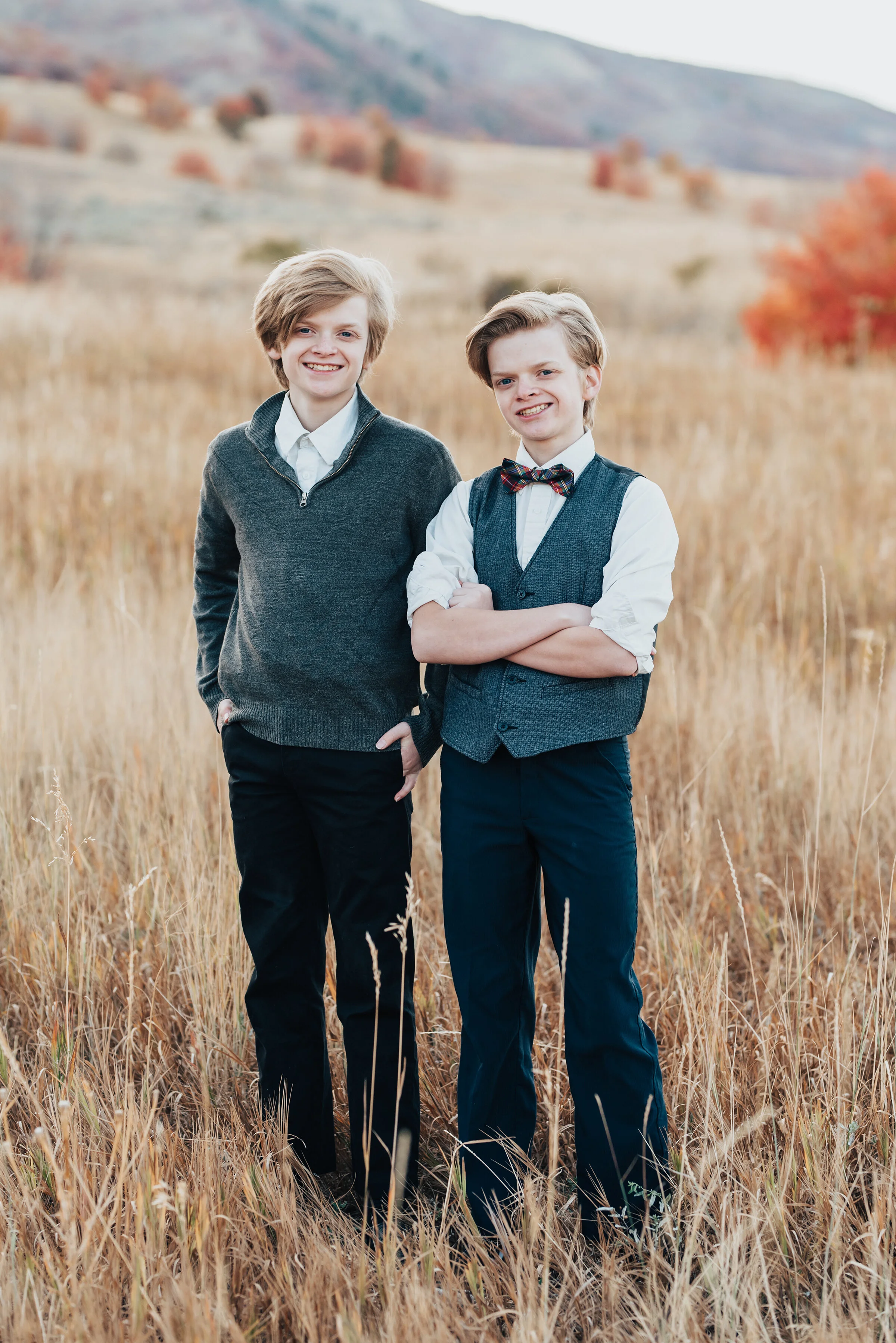  Portrait of two brothers dressed in formal clothes, standing in a field of wild grass, with mountains in background, photographed by Kristi Alyse Photography. quality wedding and family photography meaningful family photography Logan Utah photograph