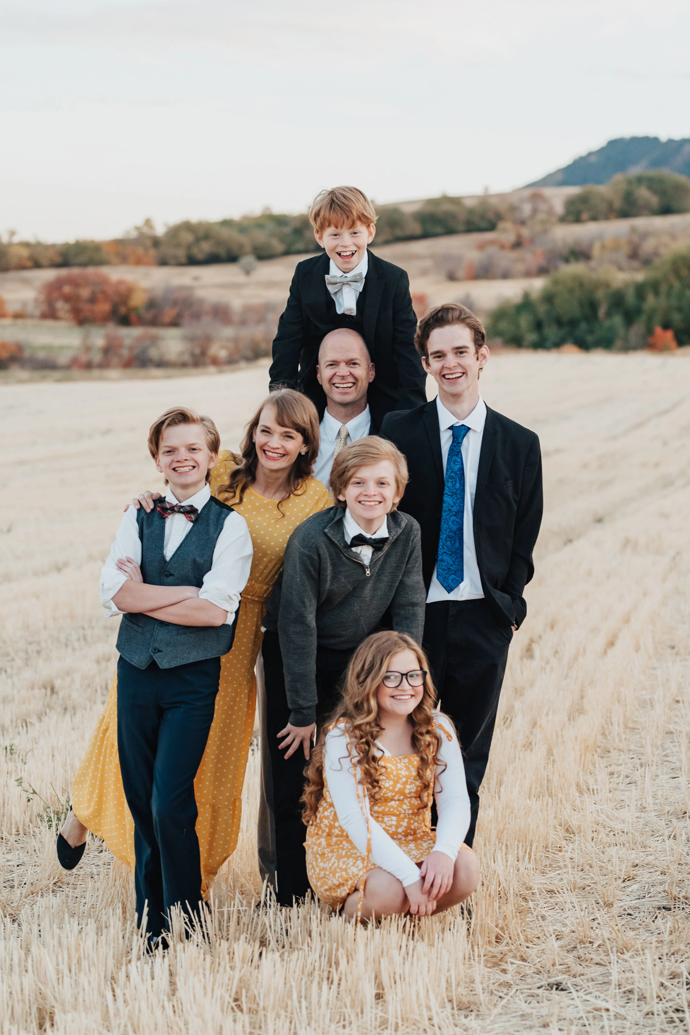  A formal family portrait in an empty farm field, the males in dark suits with white shirts while the females are in golden yellow dresses, photographed by Kristi Alyse Photography. quality wedding and family photography meaningful family photography