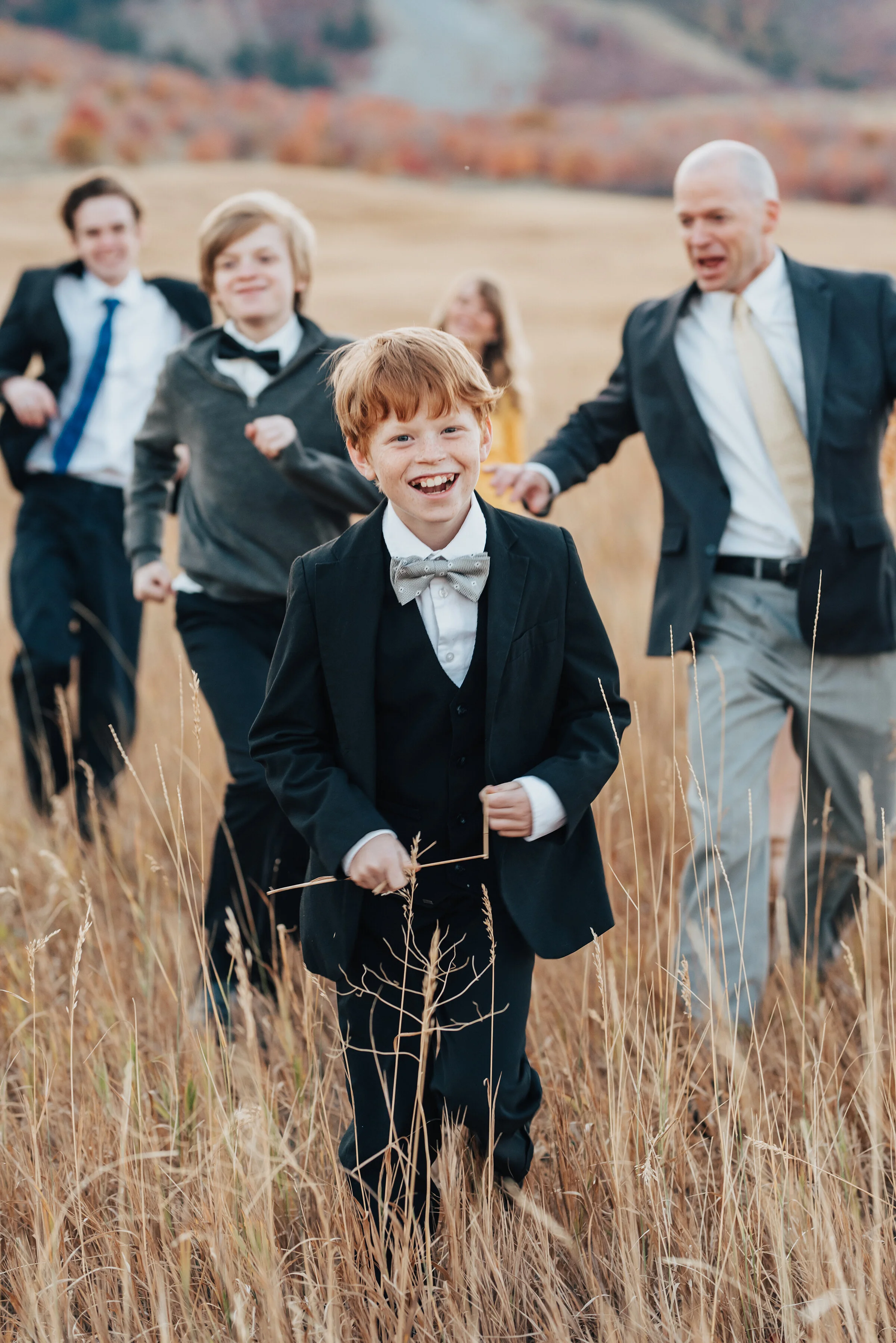  A candid portrait of a family running across an open field of wild grass, smiling and laughing, the boys in dark colours, the girls in golden yellow, photographed by Kristi Alyse Photography. quality family photography meaningful family photography 