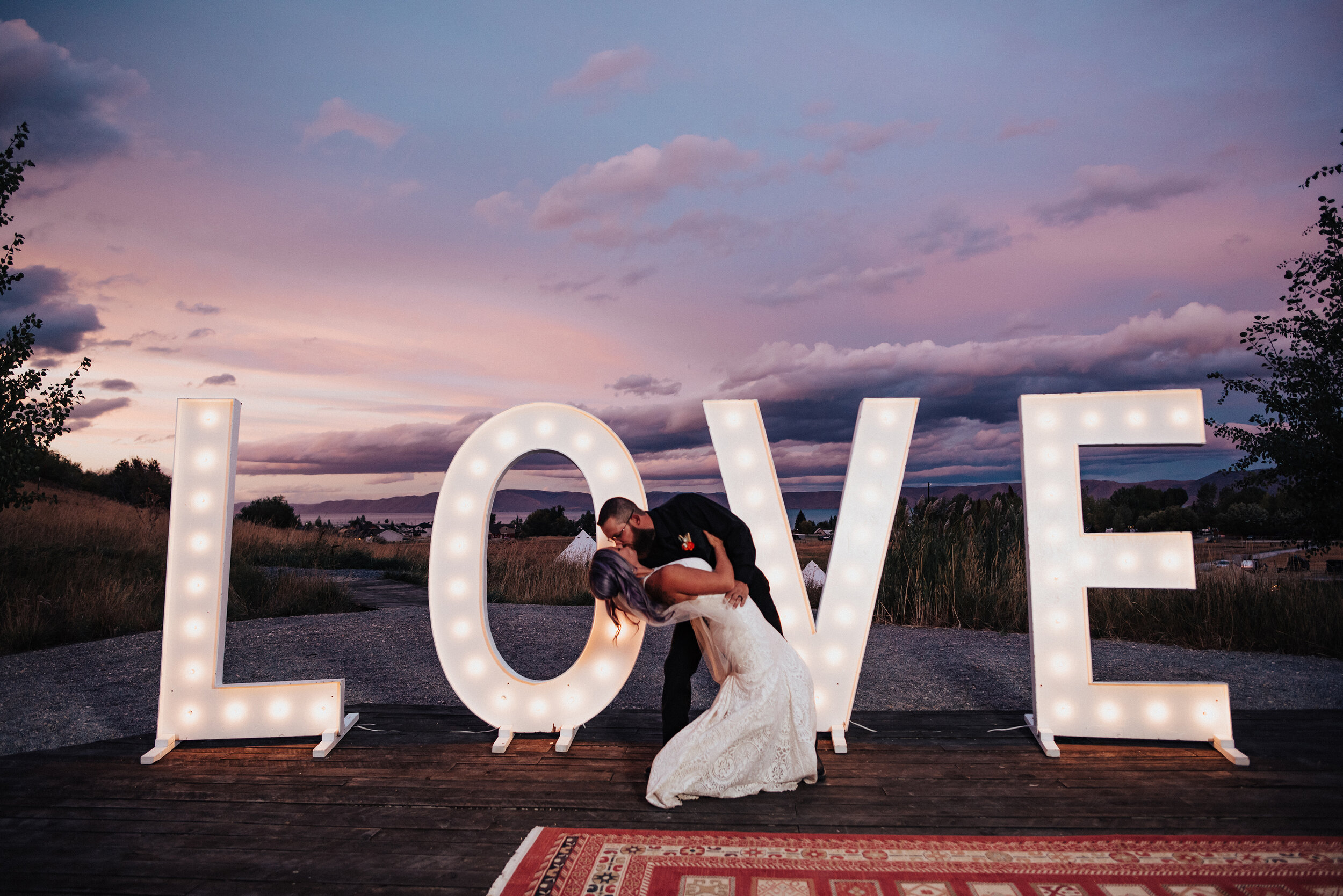 Romantic bride and groom kissing with love sign and bohemian rug in this styled shoot by Kristi Alyse Photography in Northern Utah. logan utah quality photography meaningful photography wedding and family photographer bohemian wedding love sign wedd…