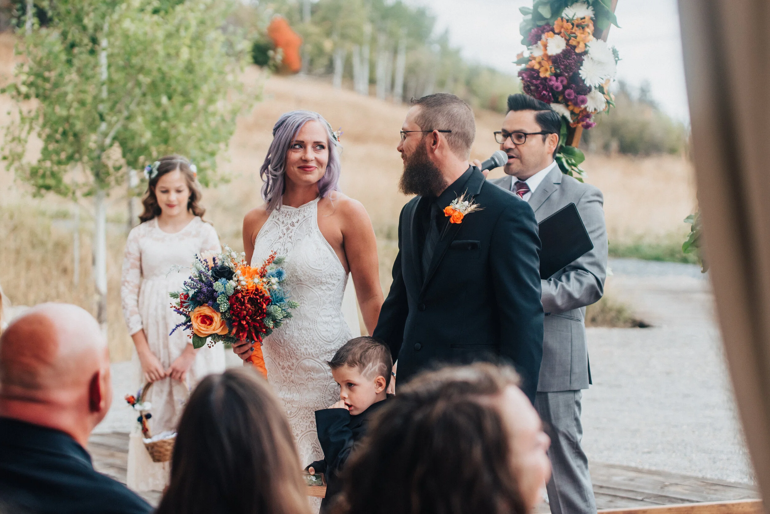 Bride with lace high collar wedding dress with purple and orange flowers and groom in black suit candid photo by Kristi Alyse Photography in Logan Utah. quality photography meaningful photography wedding and family photographer northern utah boho we…