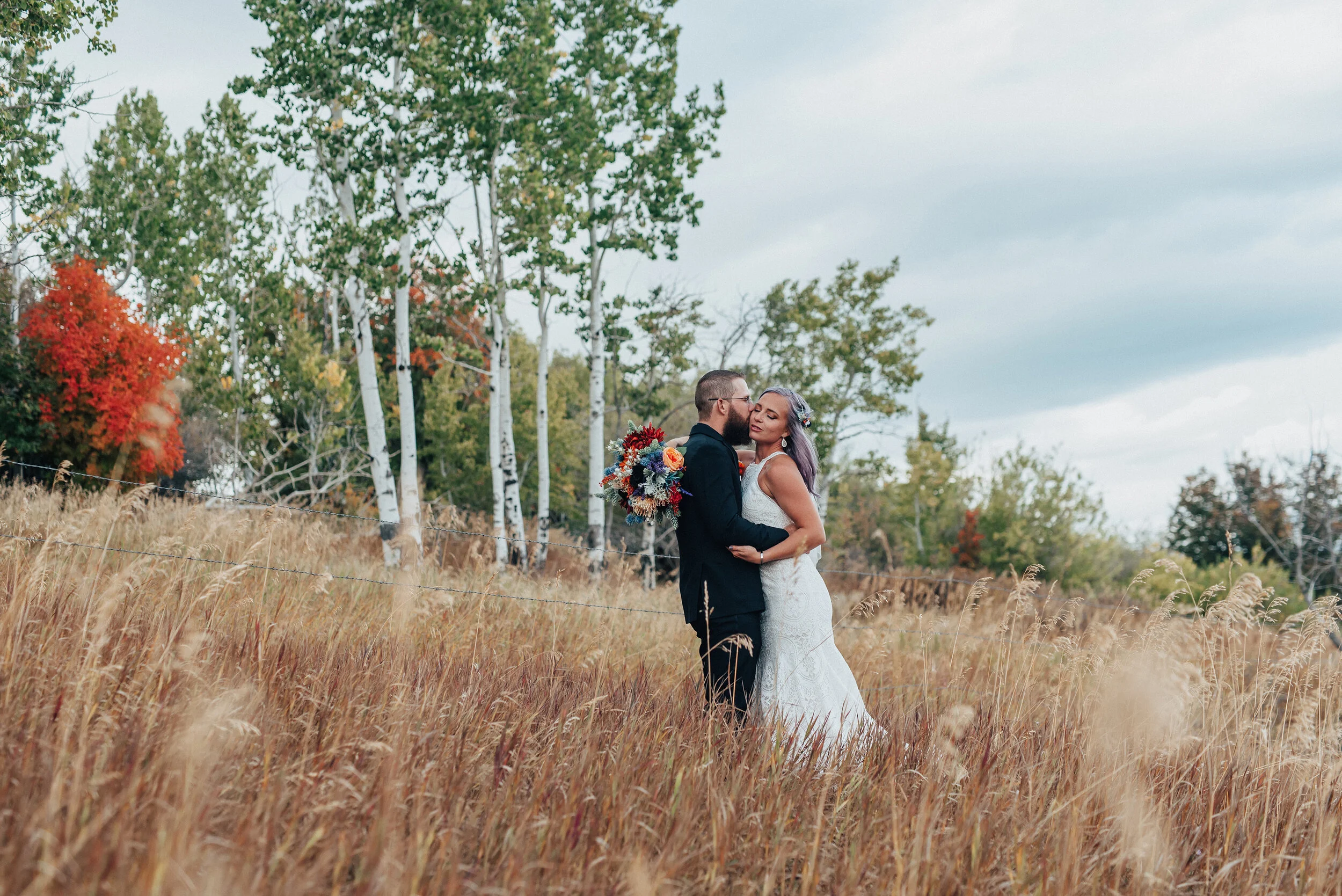 Fall styled wedding shoot in a field with bride and groom in white lace dress and black suit with orange red and blue bridal bouquet in Northern Utah by Kristi Alyse Photography. wedding and family photographer quality photography logan utah meaning…