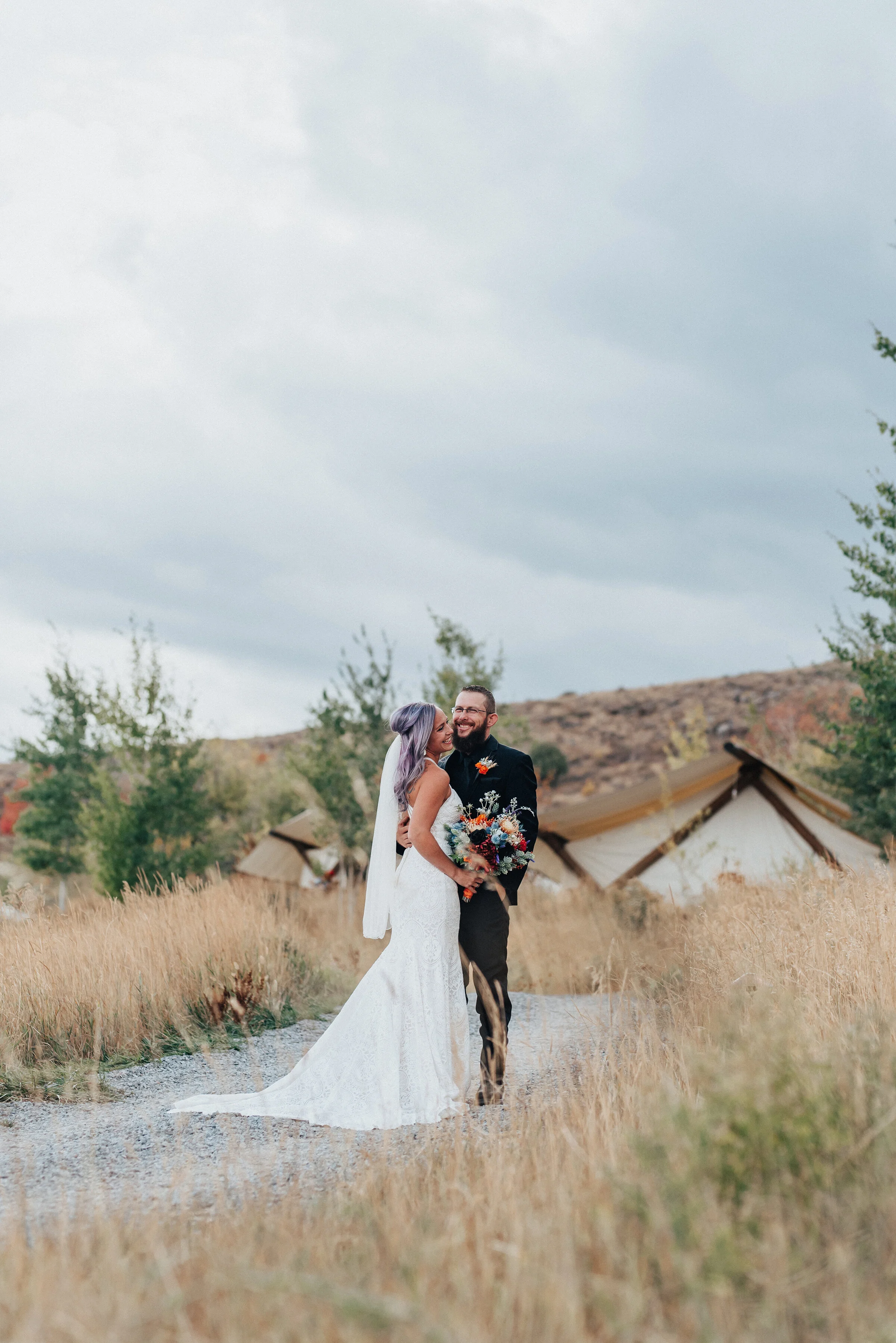  Boho styled wedding shoot with bride and groom in white lace dress with long train and black suit in Logan Utah by Kristi Alyse Photography. wedding inspo white lace dress long train purple hair black suit wedding and family photographer quality pho