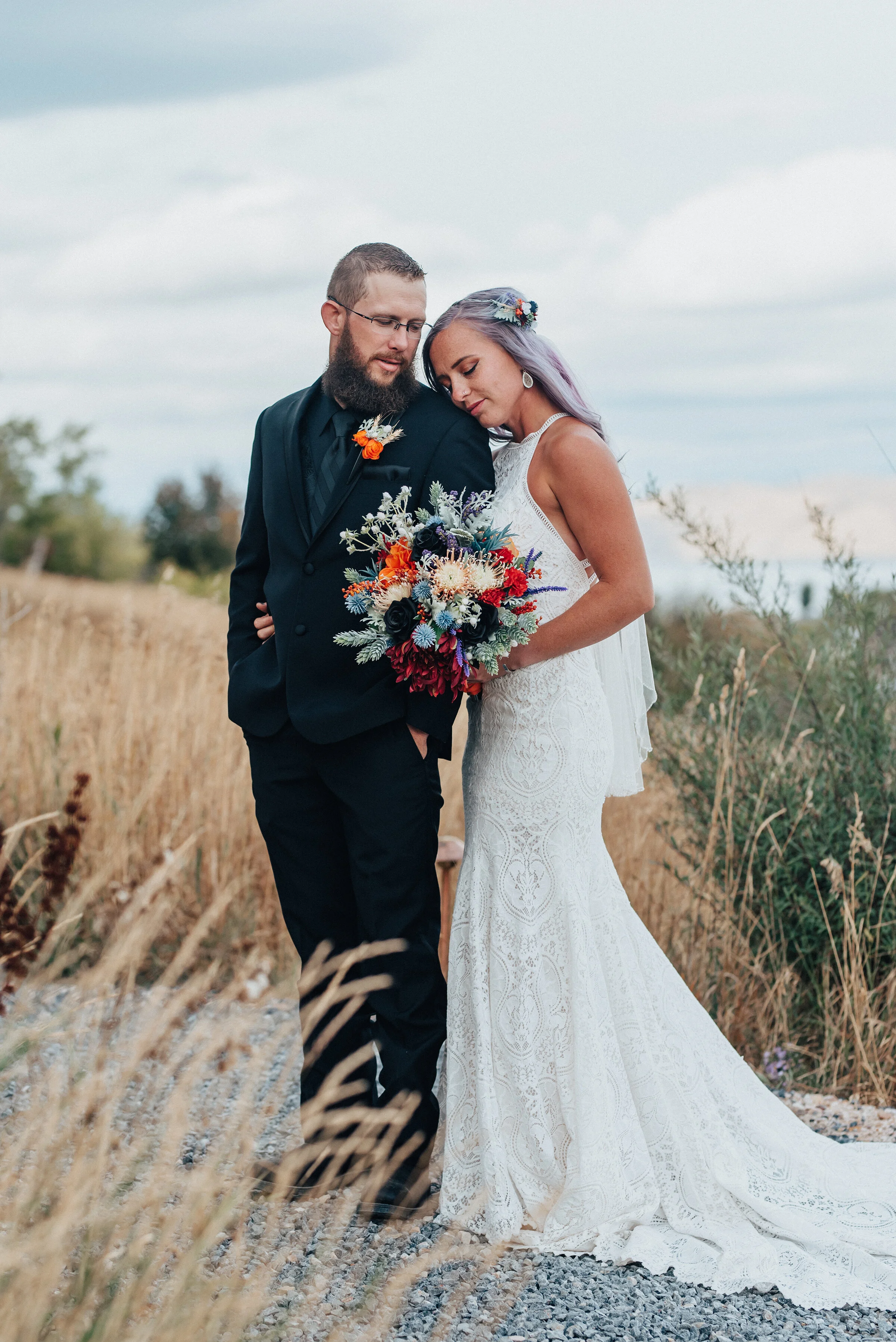  Beautiful bride with groom in lace dress with long train and black suit with orange boutonniere in this boho styled shoot by Kristi Alyse Photography in Northern Utah. black suit lace dress long train purple hair northern utah quality photography me
