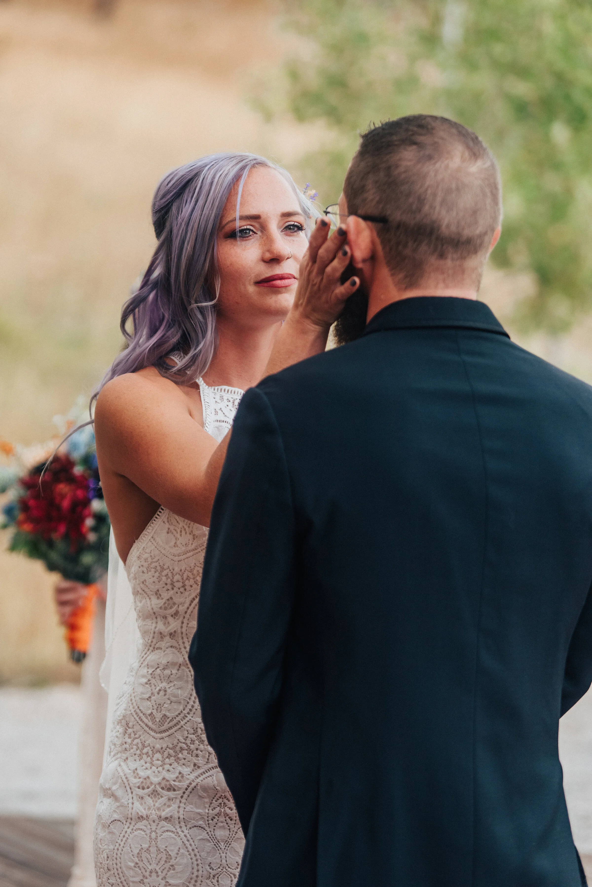  Candid photo of bride with purple hair and lace white dress with dark red flower bouquet and groom in black suit by Kristi Alyse Photography in Logan Utah. meaningful photography wedding and family photographer boho wedding dark red bridal bouquet f