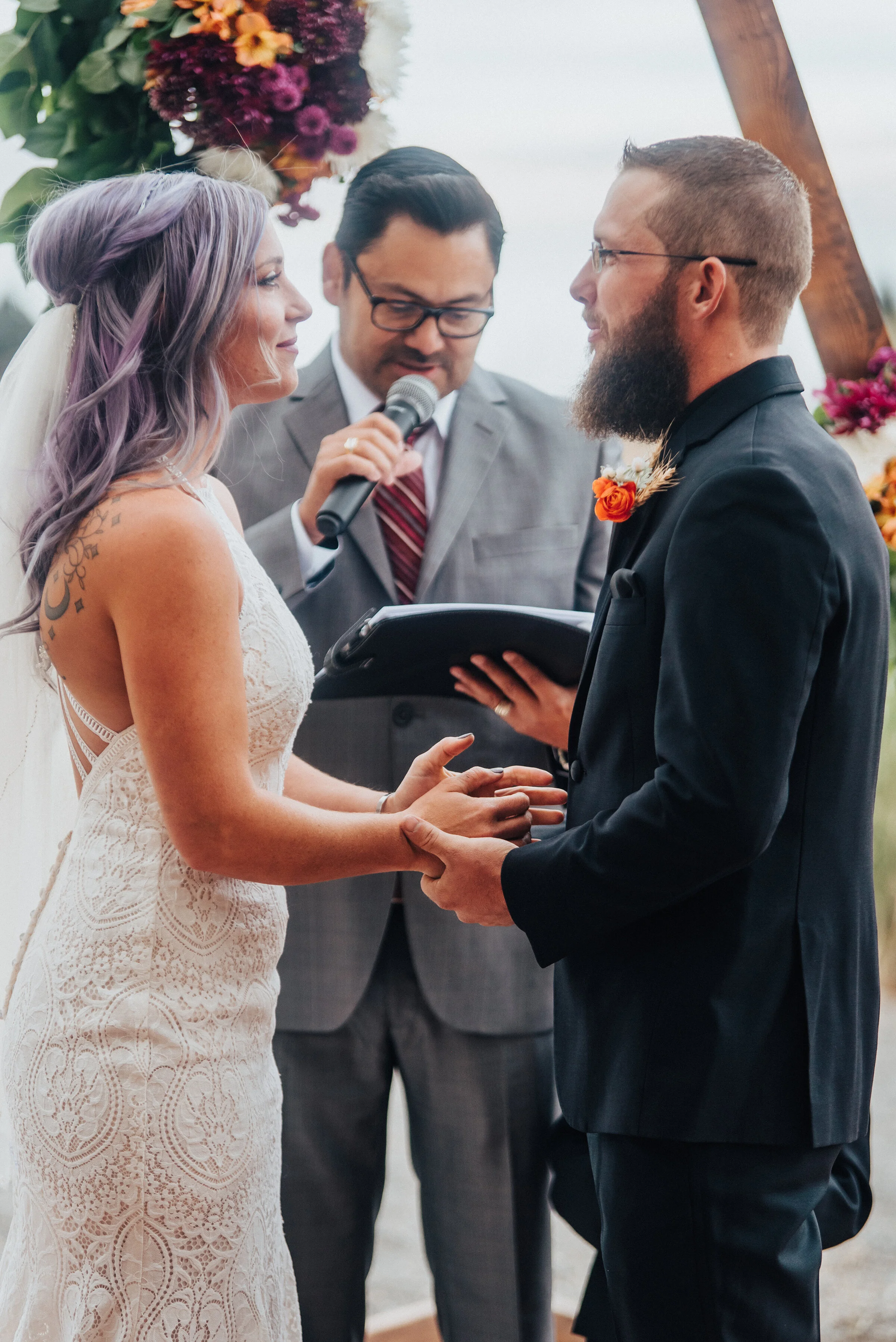  Groom and bride at the altar with purple hair and lace dress and black suit with dark purple and orange floral decor in this boho candid wedding photo by Kristi Alyse Photography in Northern Utah. boho wedding altar dark purple orange flowers lace d