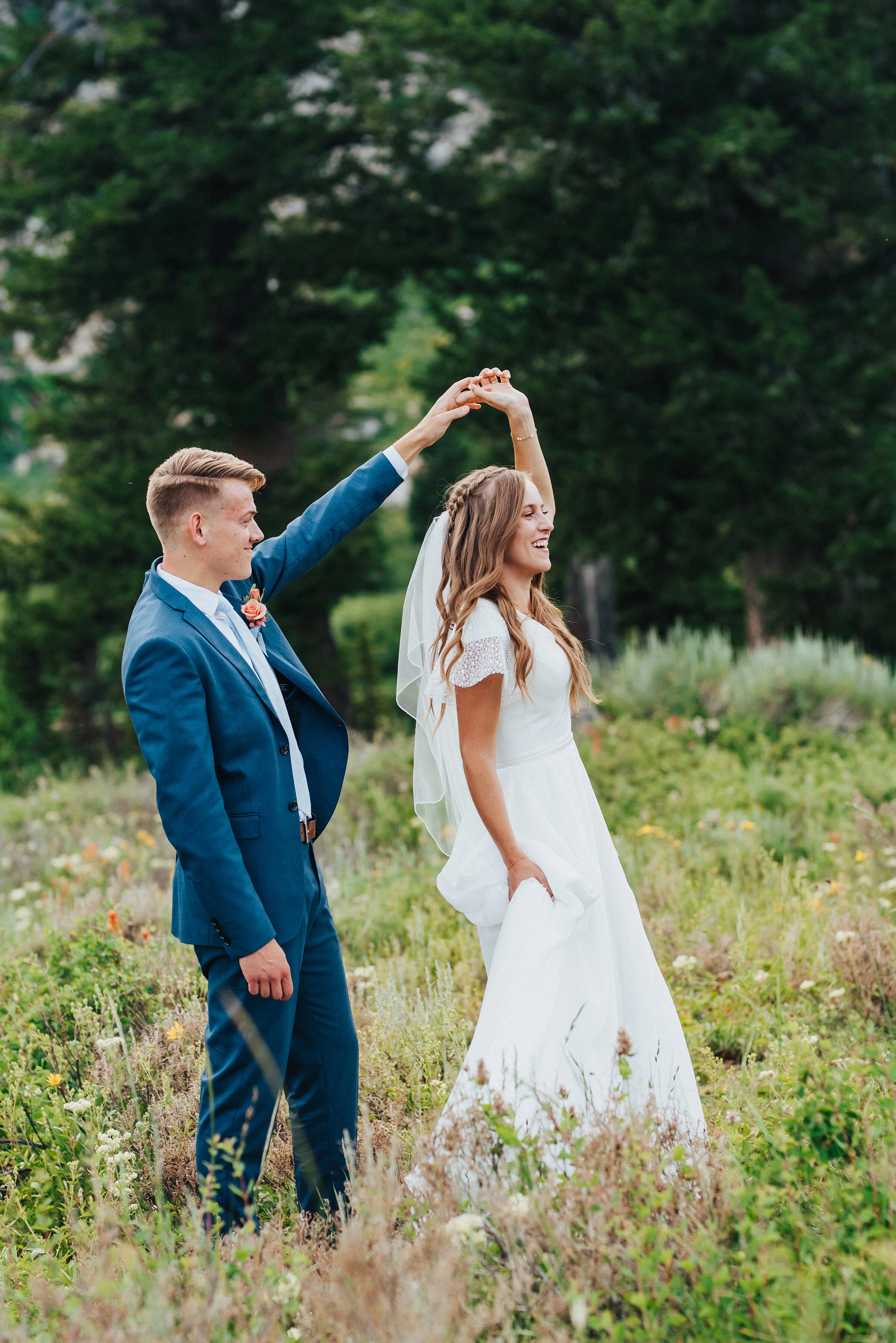  Handsome groom in a blue suit twirling his stunning bride wearing a modest wedding dress in the green pine forest of Tony Grove in Northern Utah. Wedding formals in the mountain unique wedding photography inspo groom in a blue suit first dance for t