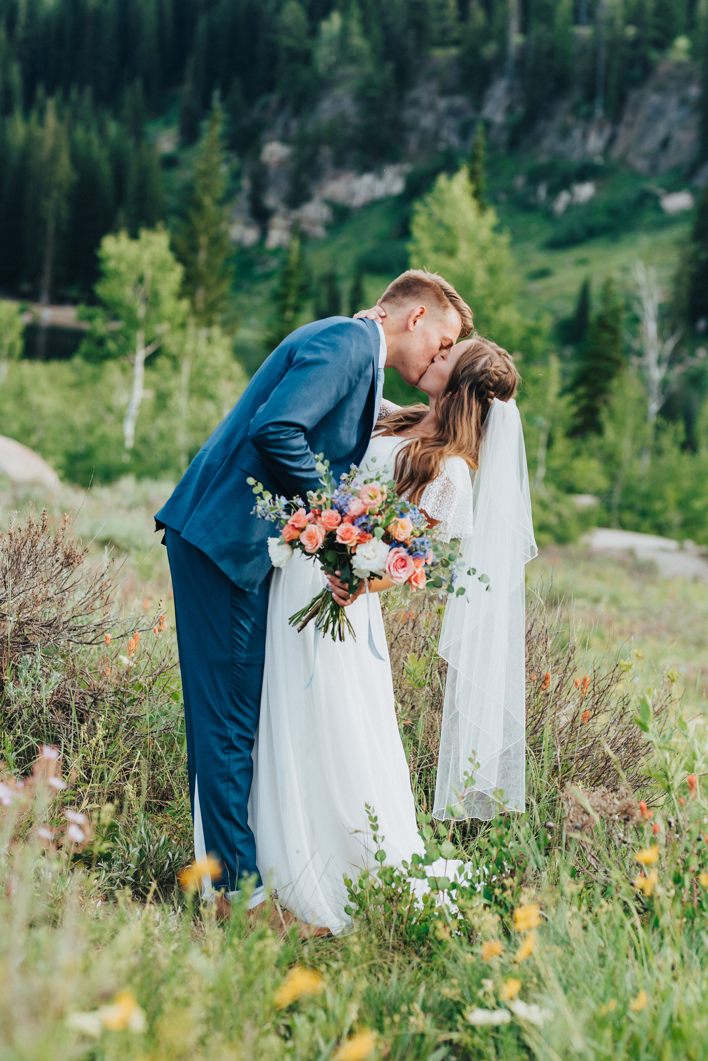  Close-up shot of a bride and groom kissing accenting her cascading hair with the veil tucked into her braid&nbsp; while holding her bridal bouquet. Northern utah wedding photography boutineer for the groom bridal bouquet inspo wedding veil hair and 