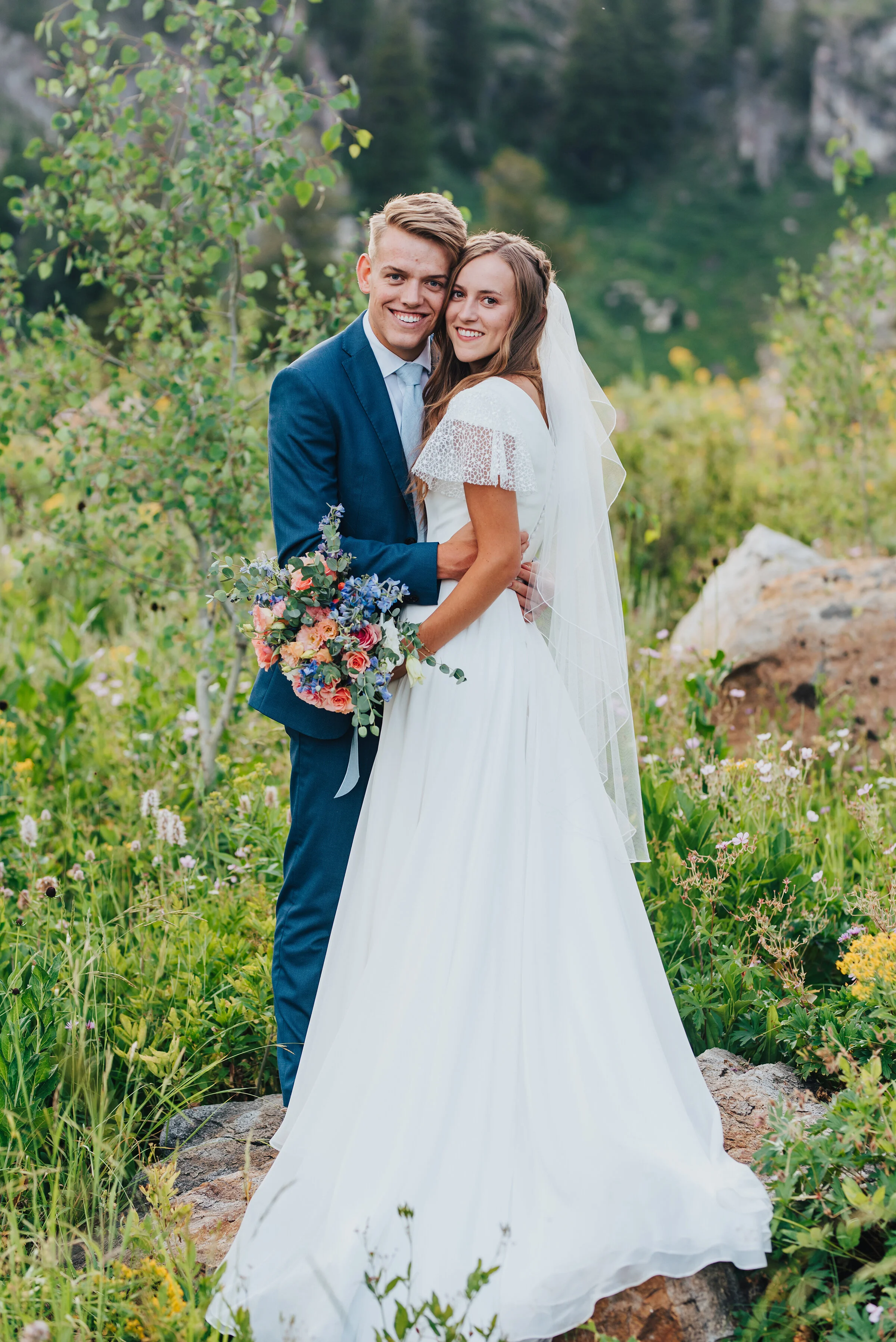  Handsome groom in a blue suit holding his bride while she holds a beautiful spring bridal bouquet. Northern Utah wedding photography utah bride and groom modest wedding dress spring bridal bouquet inspo groom in a blue suit wedding veil inspo #weddi