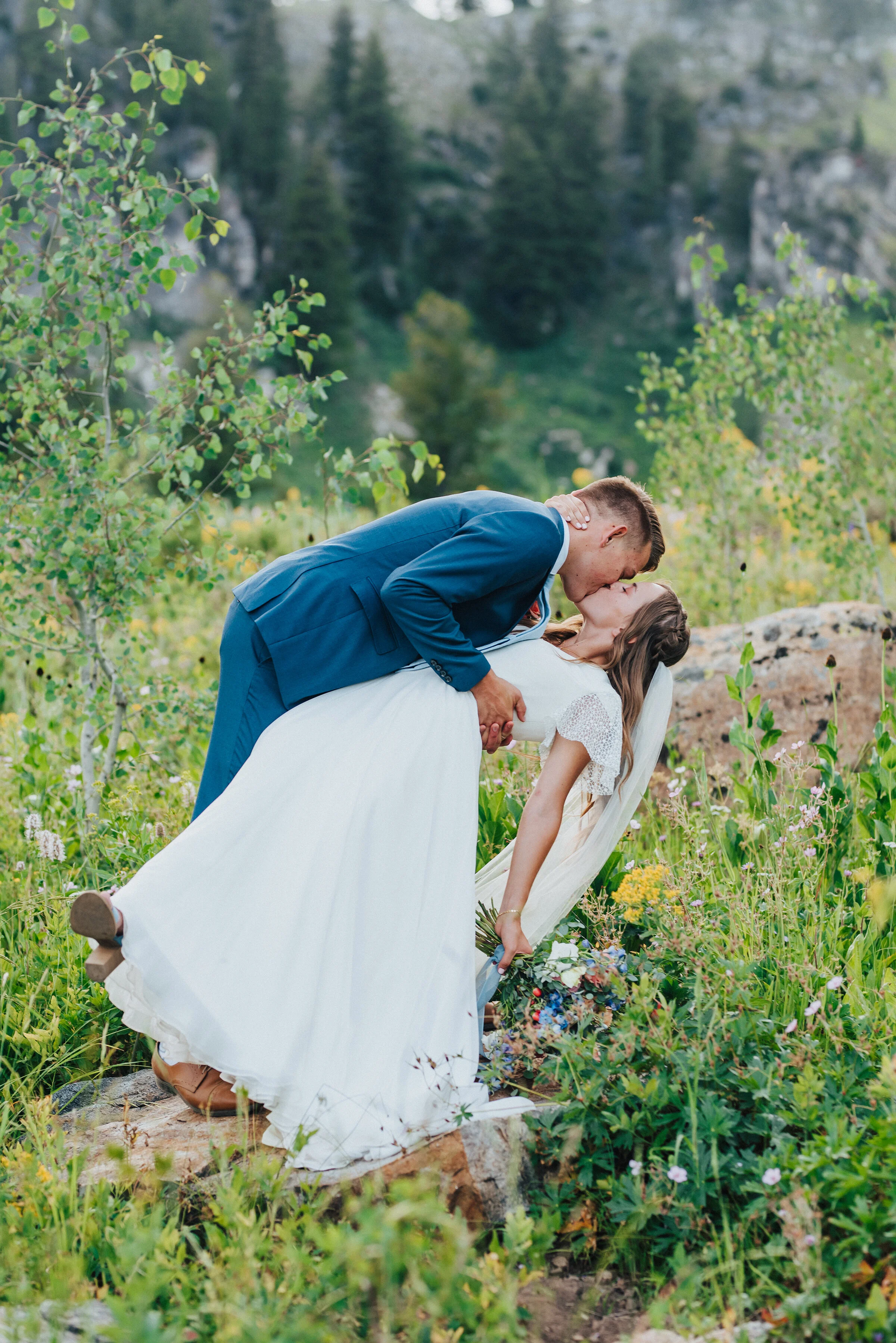  Gorgeous bride holding a wildflower wedding bouquet while her groom dips her in a kiss at Tony Grove in northern Utah for a formal wedding photography session. Wedding photography in northern utah wedding formals at tony grove dip kiss wedding photo