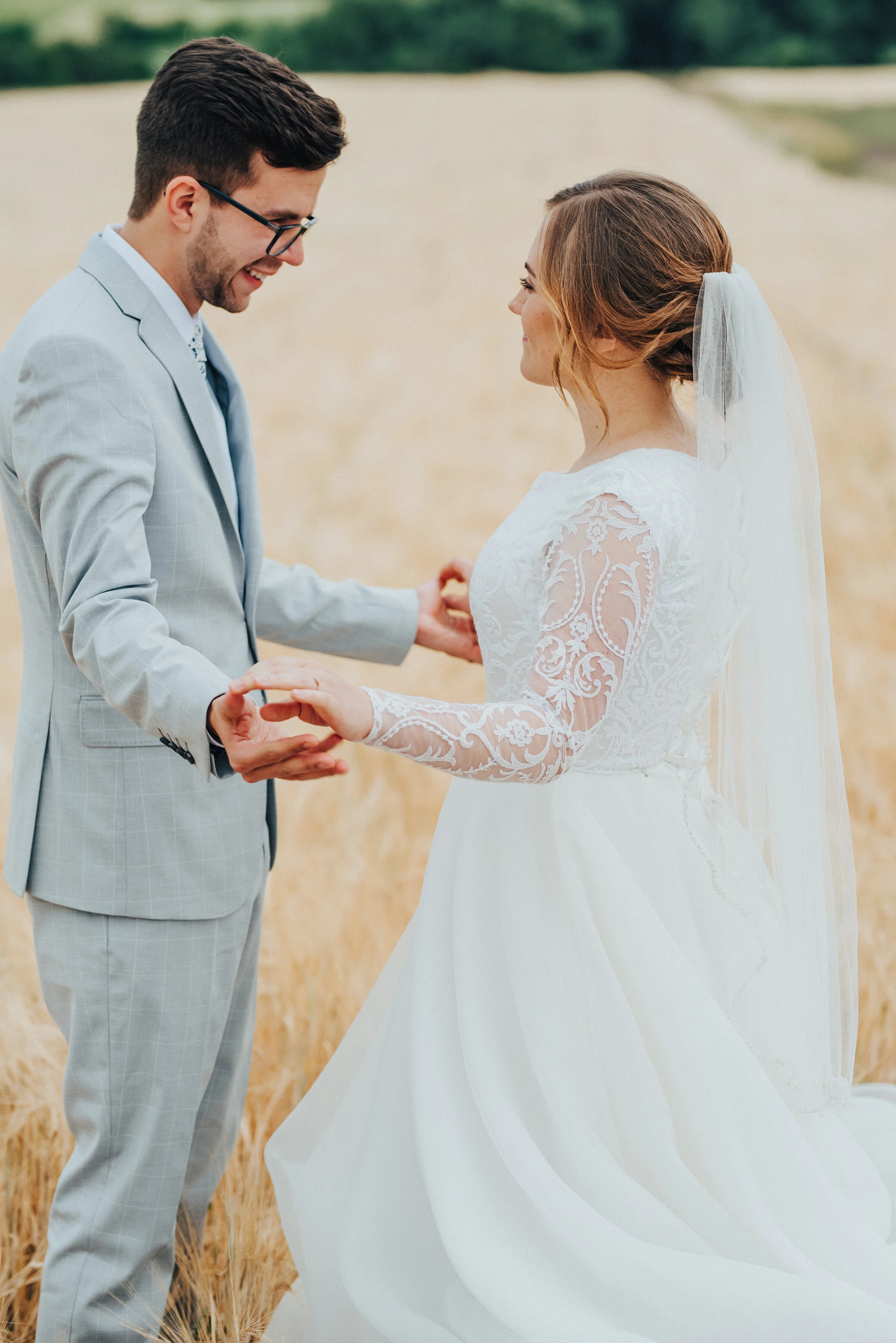  This photo taken by Kristi Alyse Photography in Cache Valley, Utah encompasses pure contentment as the bride and groom share their first look. holding hands bride and groom, tall grass bridal session, floor-length bridal veil, light gray plaid weddi
